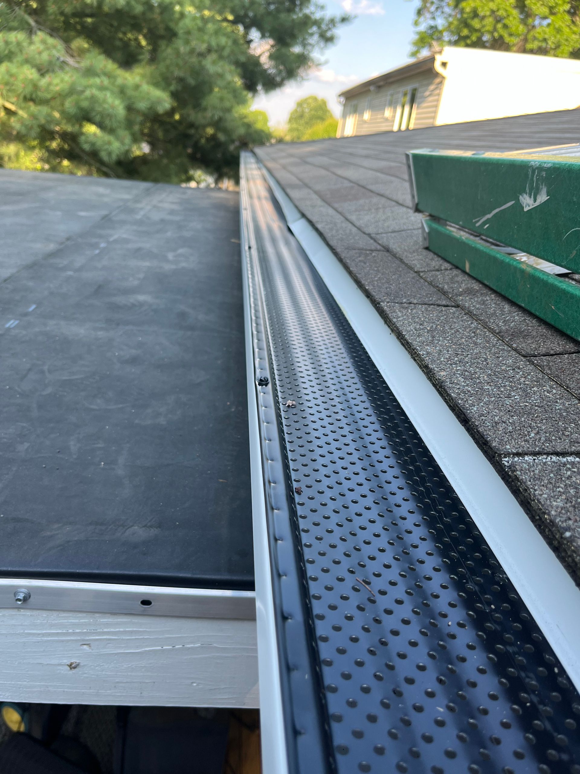 Roof edge with metal gutter and black shingles beside a rooftop vent box