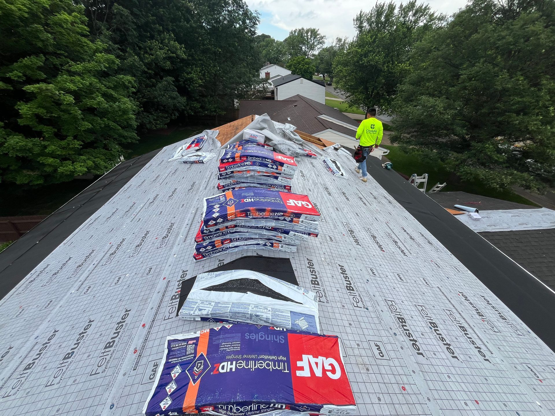 Roof under repair with bright underlayment and worker in neon jacket on the ridge
