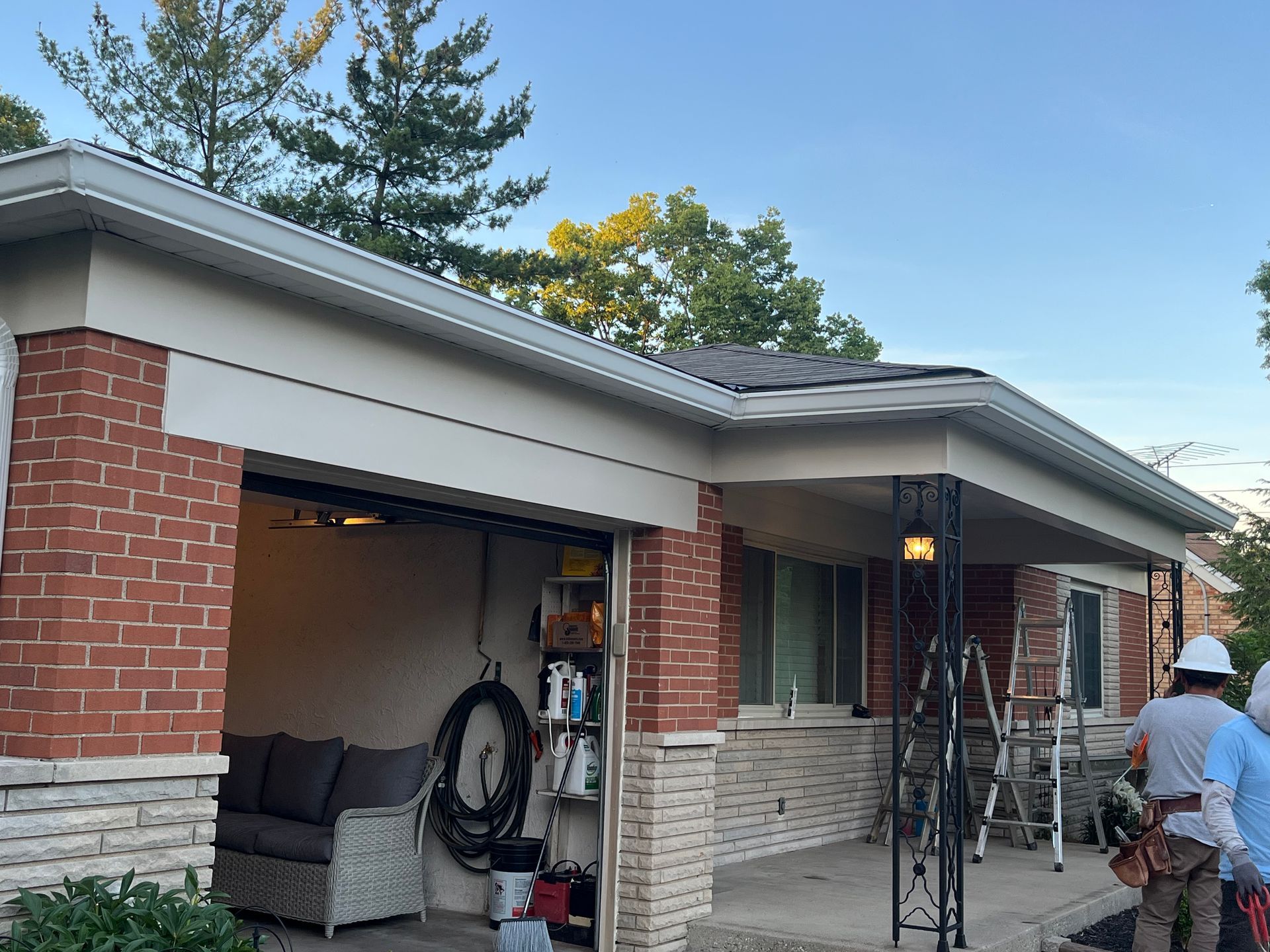 Workers on ladders painting the exterior of a brick house with a gray roof.