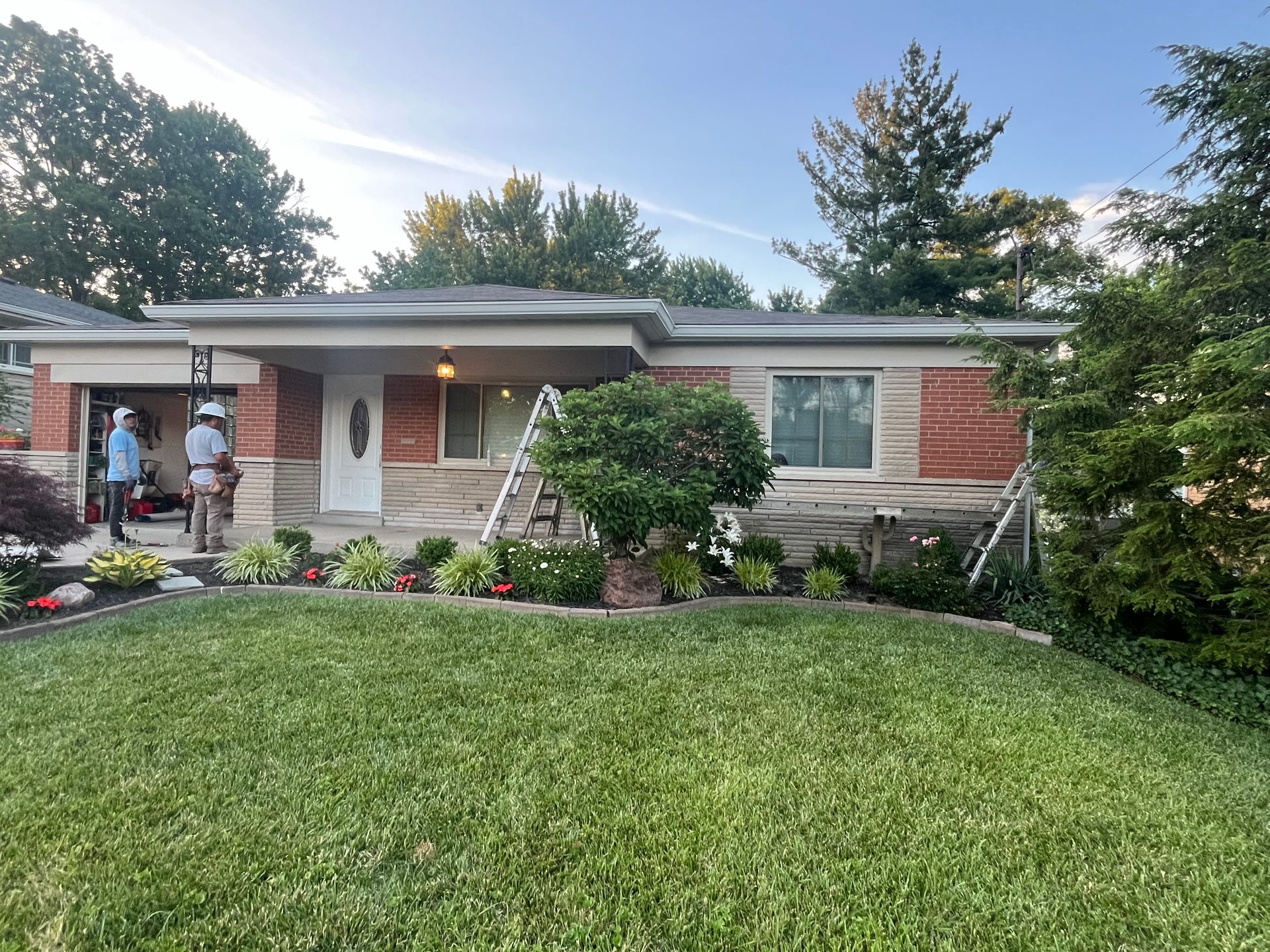 Single-story brick house with a green lawn, front porch, and two people near the entrance.