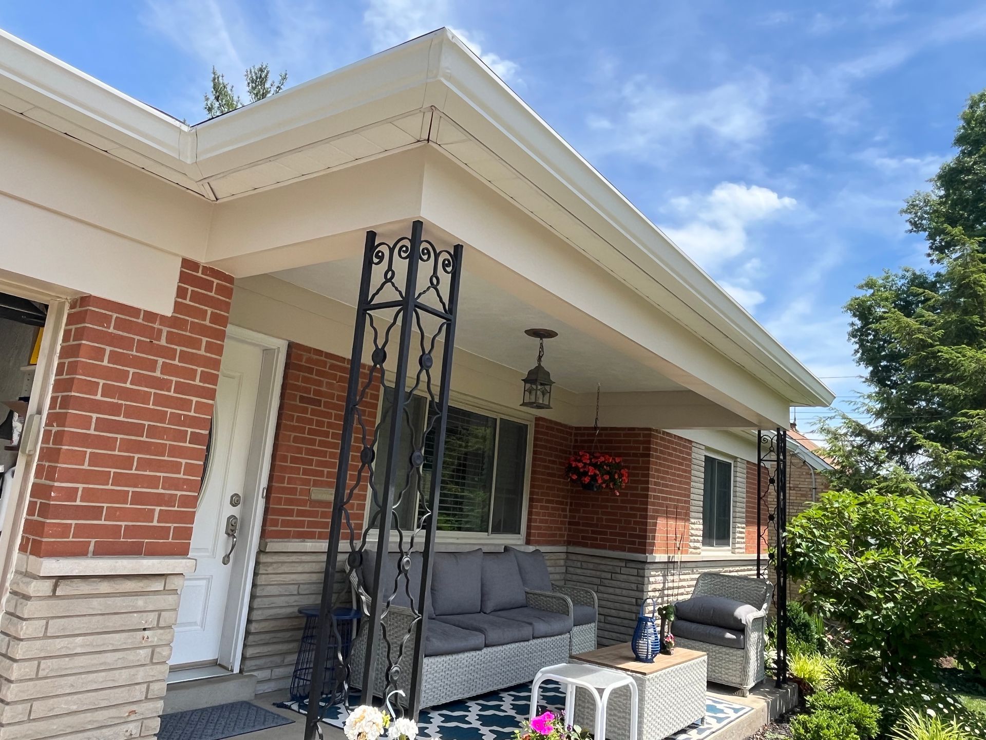 Front porch with red brick columns, gray chairs, and a decorative black support post under a white roof.