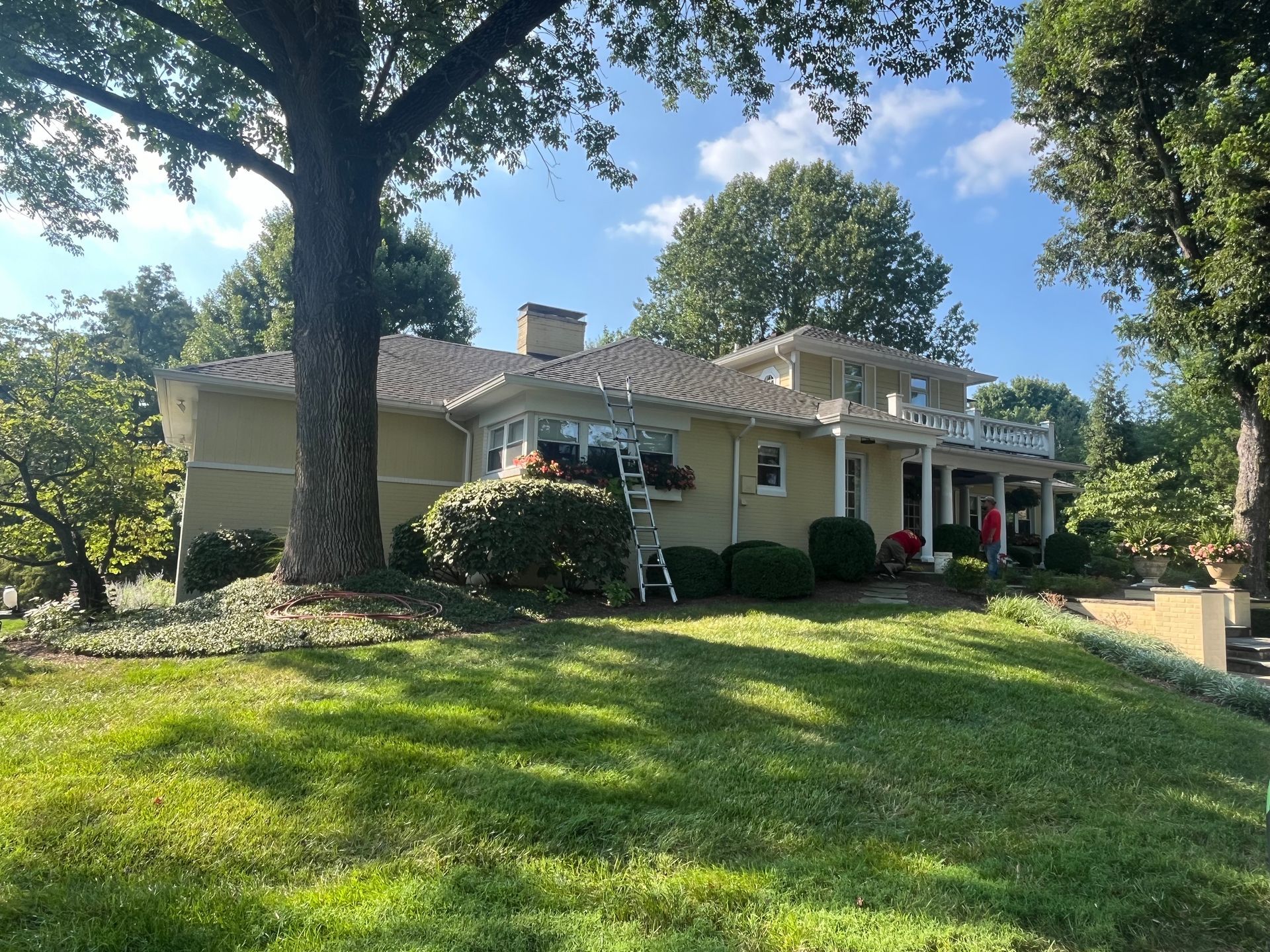 Suburban house with white columns, red front door, and a green lawn under tall trees
