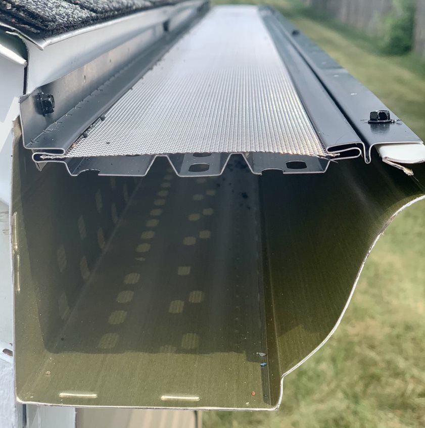 Close-up of a black metal roof gutter with a perforated leaf guard on top
