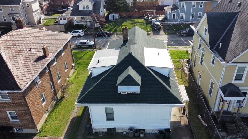 Aerial view of a white house with a dark roof on a residential street, surrounded by neighboring homes.