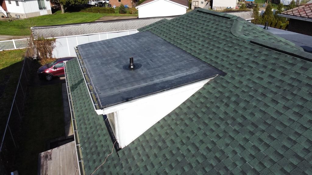 House roof with dark flat-roof addition and green shingle roof, viewed from above