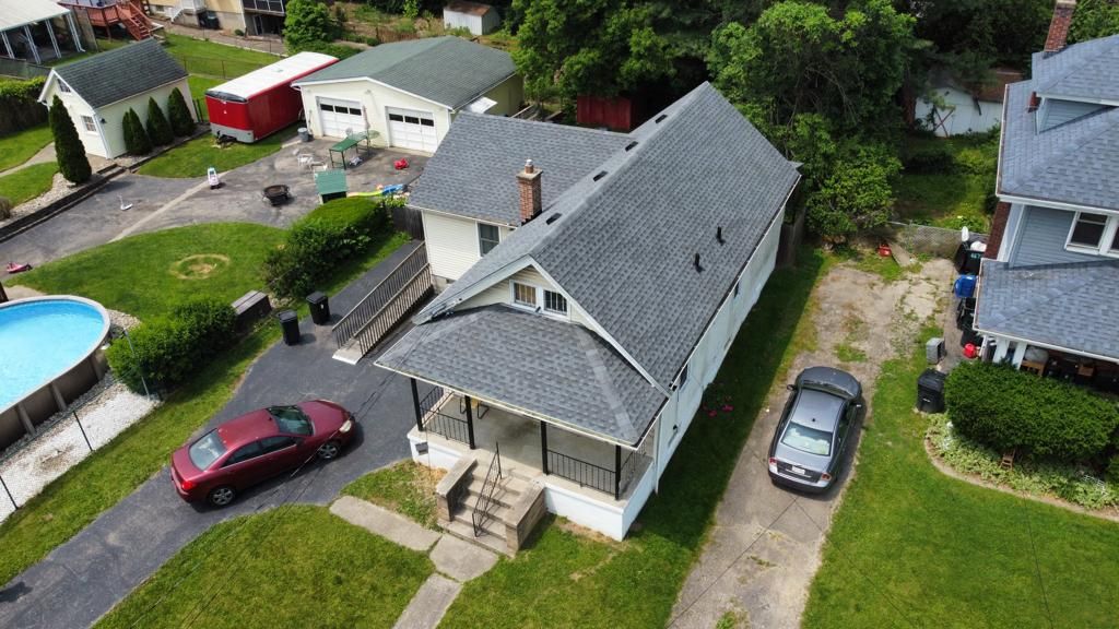 Aerial view of a gray house with two parked cars, a driveway, lawn, and a backyard pool.