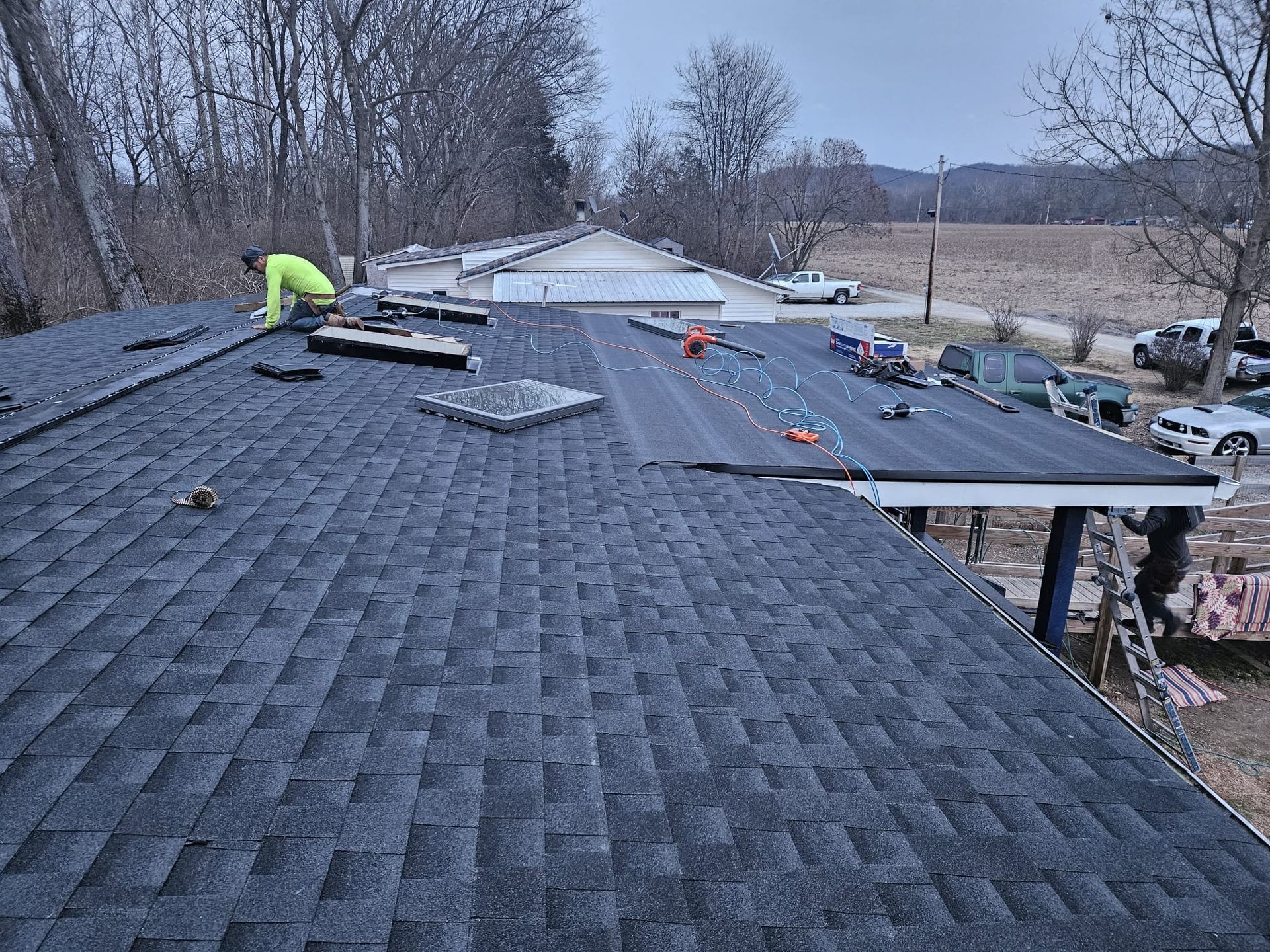 Worker installing shingles on a roof under repair, with materials spread across the rooftop.