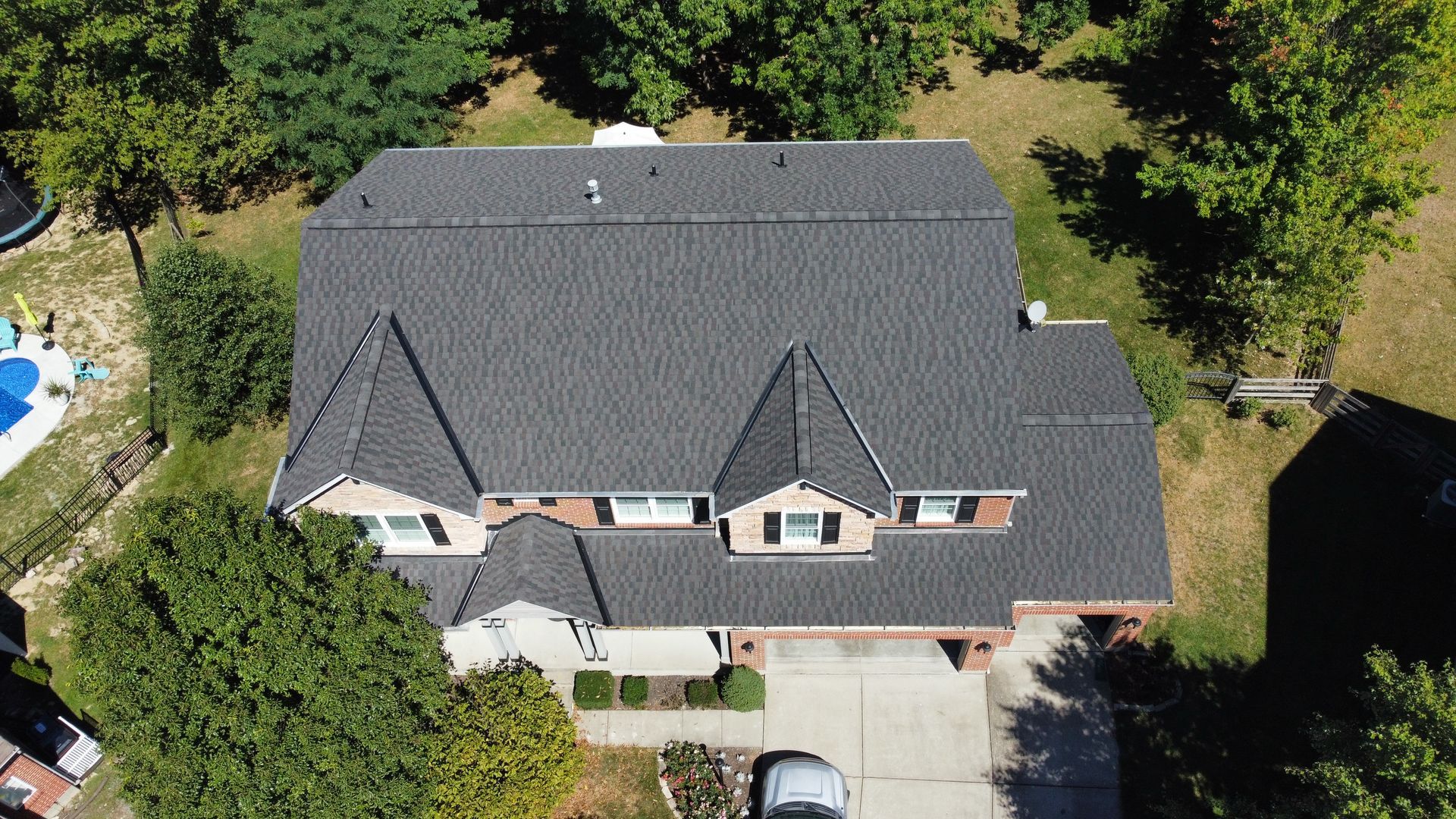 Aerial view of a gray-shingled suburban house with a driveway and surrounding trees.