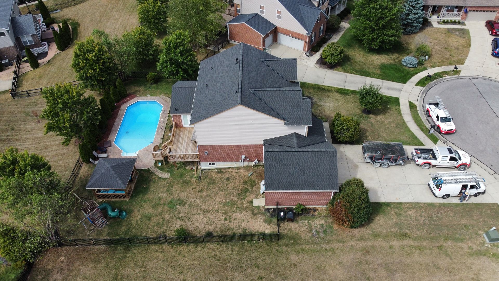 Aerial view of a suburban house with a backyard pool, driveway, and parked vehicles.