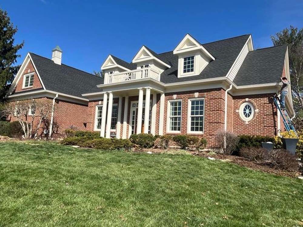 A large brick house with a black roof is sitting on top of a lush green lawn.