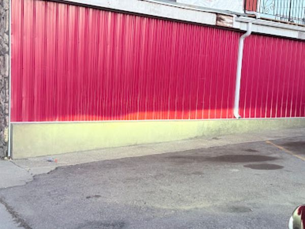 Red corrugated metal wall with a light yellow base. A white gutter is visible.