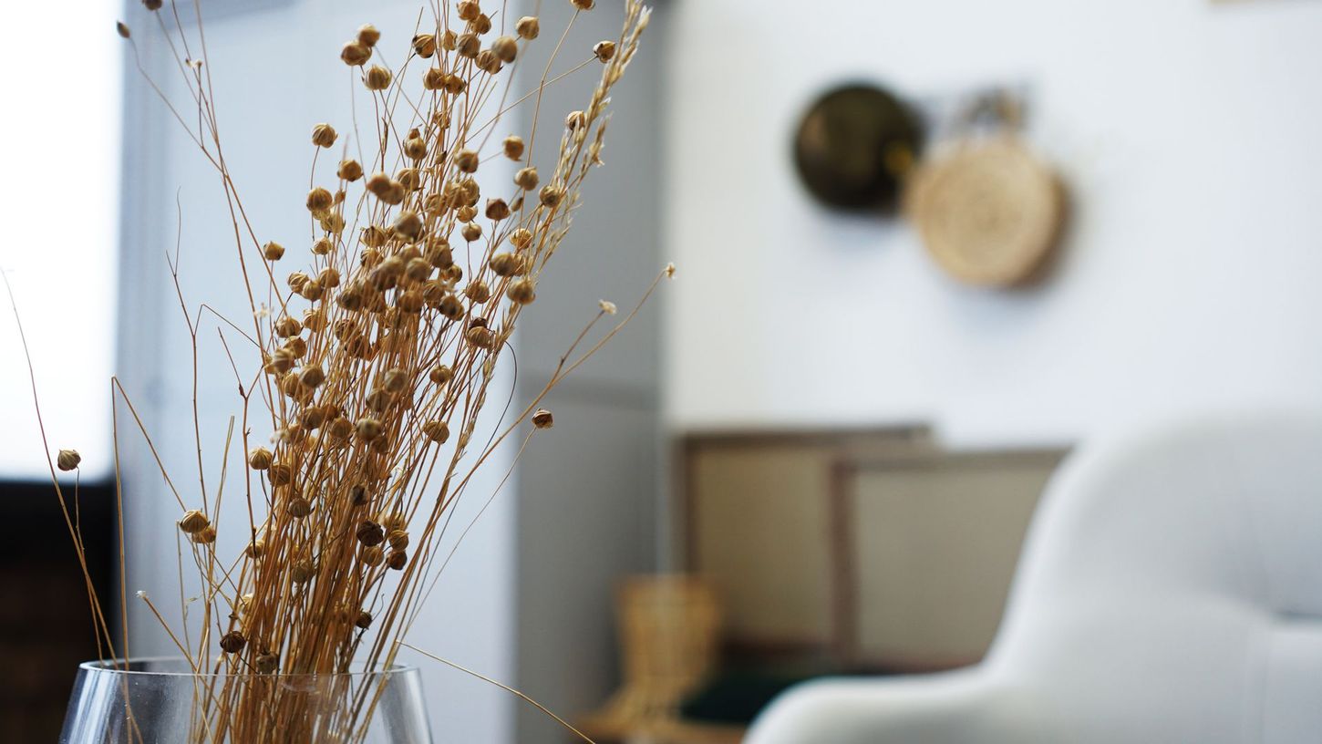 Dried flowers in a vase beside a white chair in a softly lit room