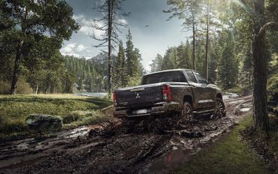 SUV vermelha atravessando águas rasas com ondas quebrando em uma paisagem montanhosa acidentada.