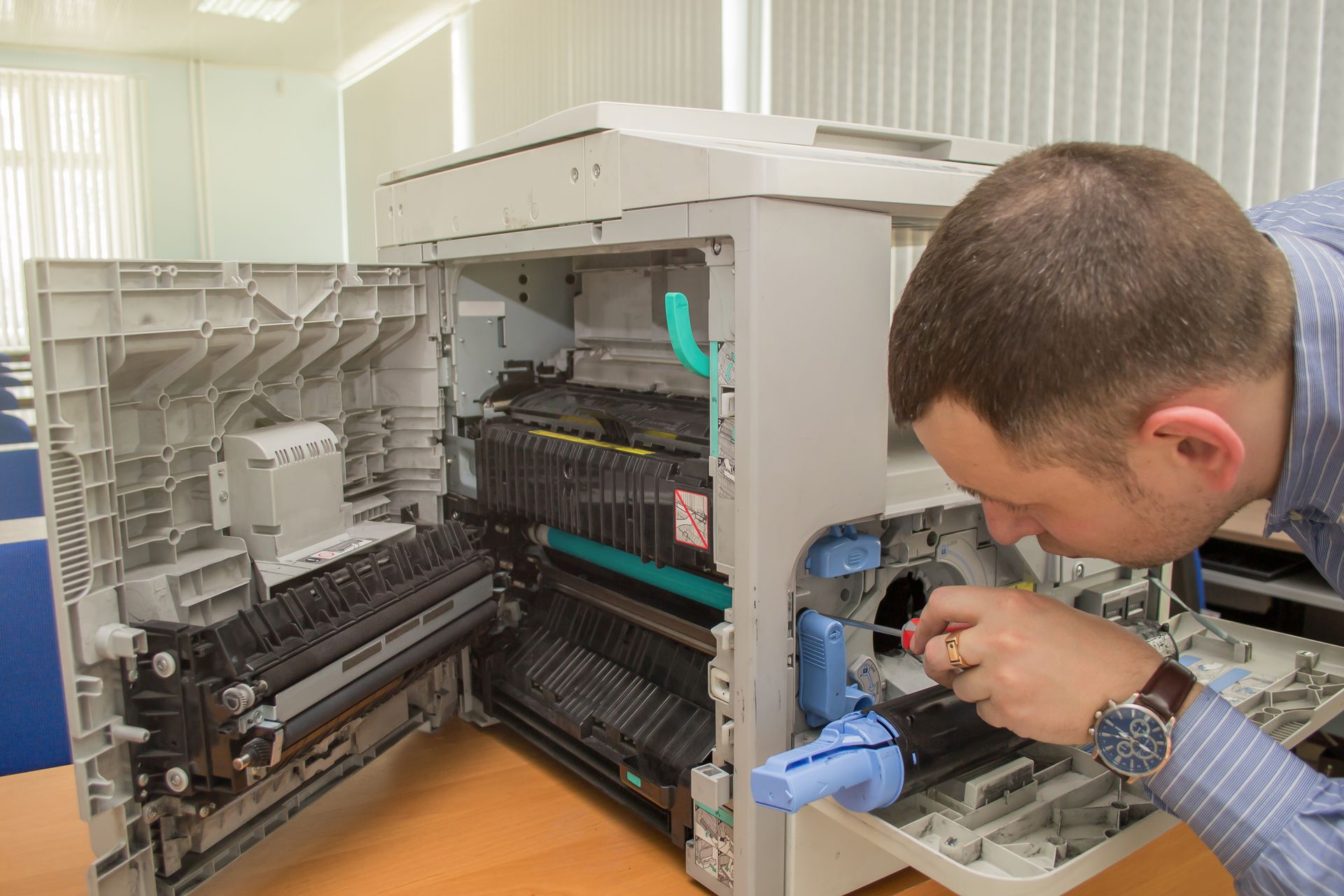 A technician working on an open copier's internal components with a screwdriver in hand