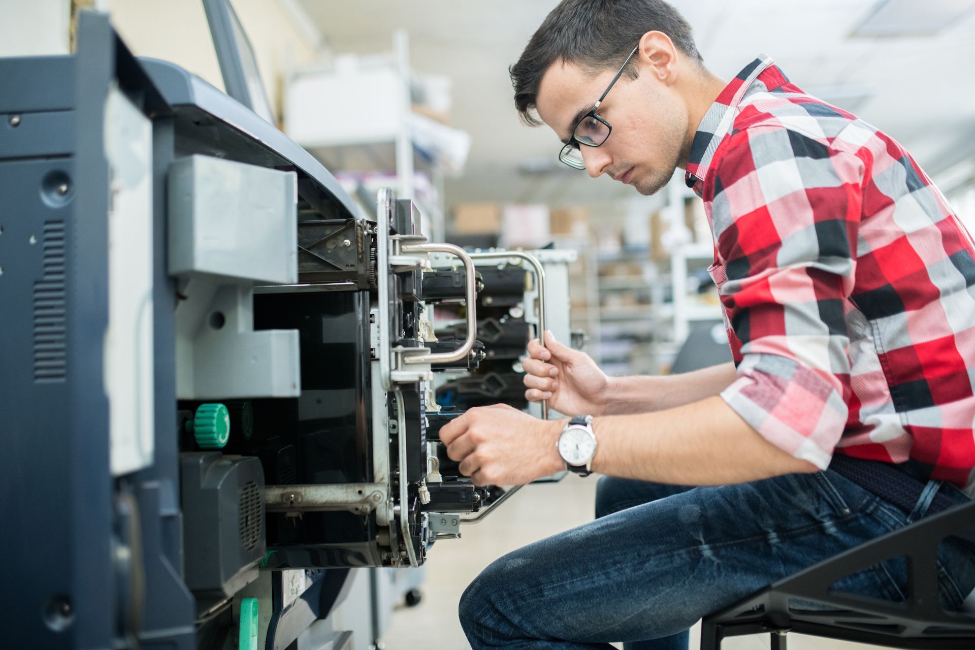 Technician servicing industrial printing equipment in a workshop or production facility. Technician servicing industrial printing equipment in a workshop or production facility.