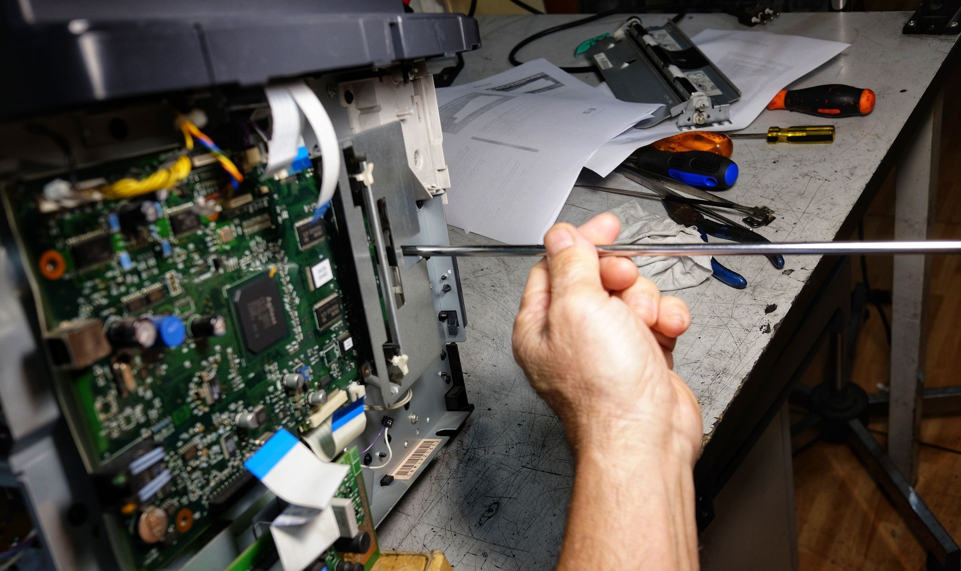 A technician repairing a copier circuit board with a screwdriver on a workbench