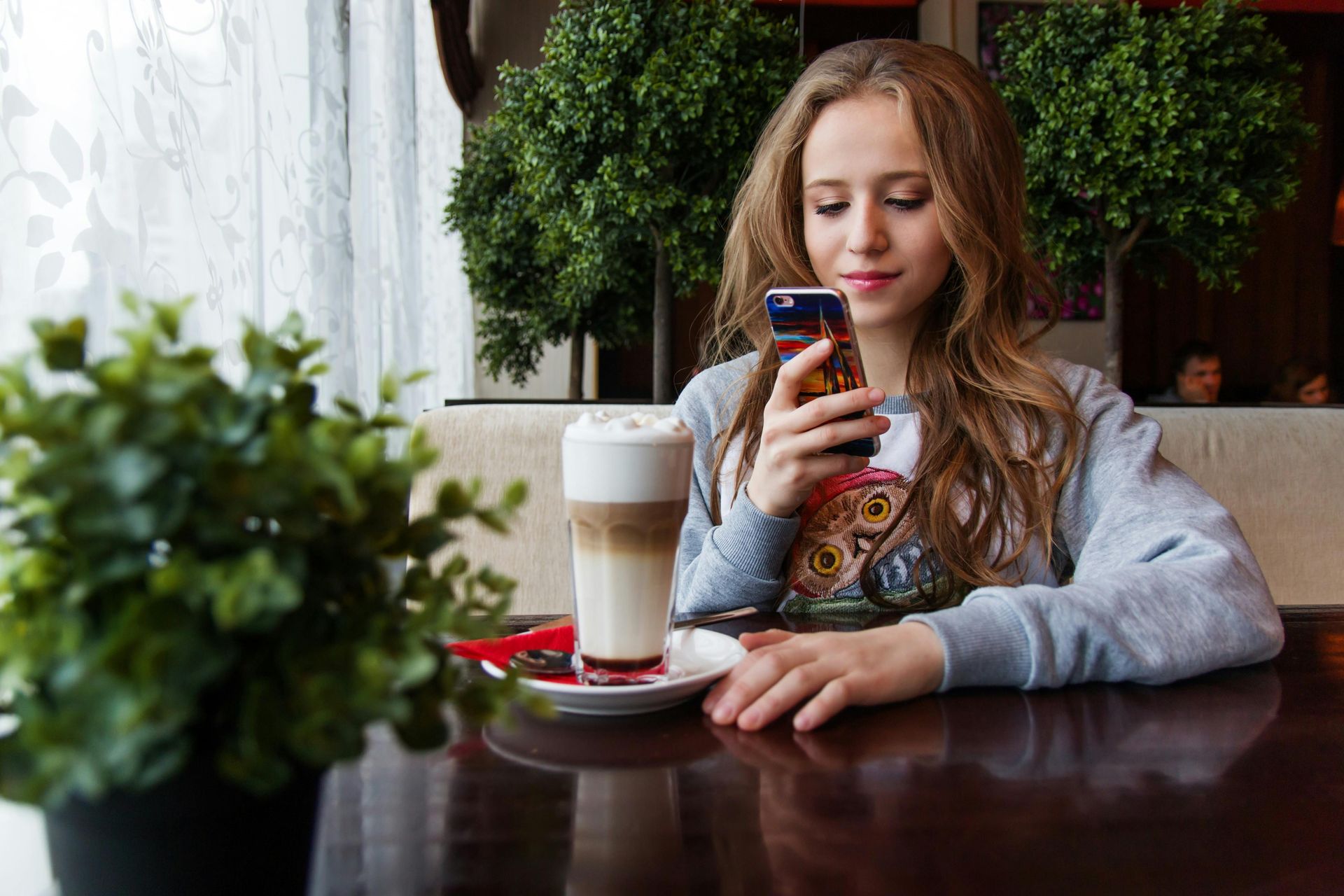 A teenage on their phone with a coffee in front of them.
