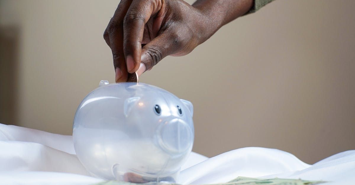 A hand putting money in a white piggy bank.
