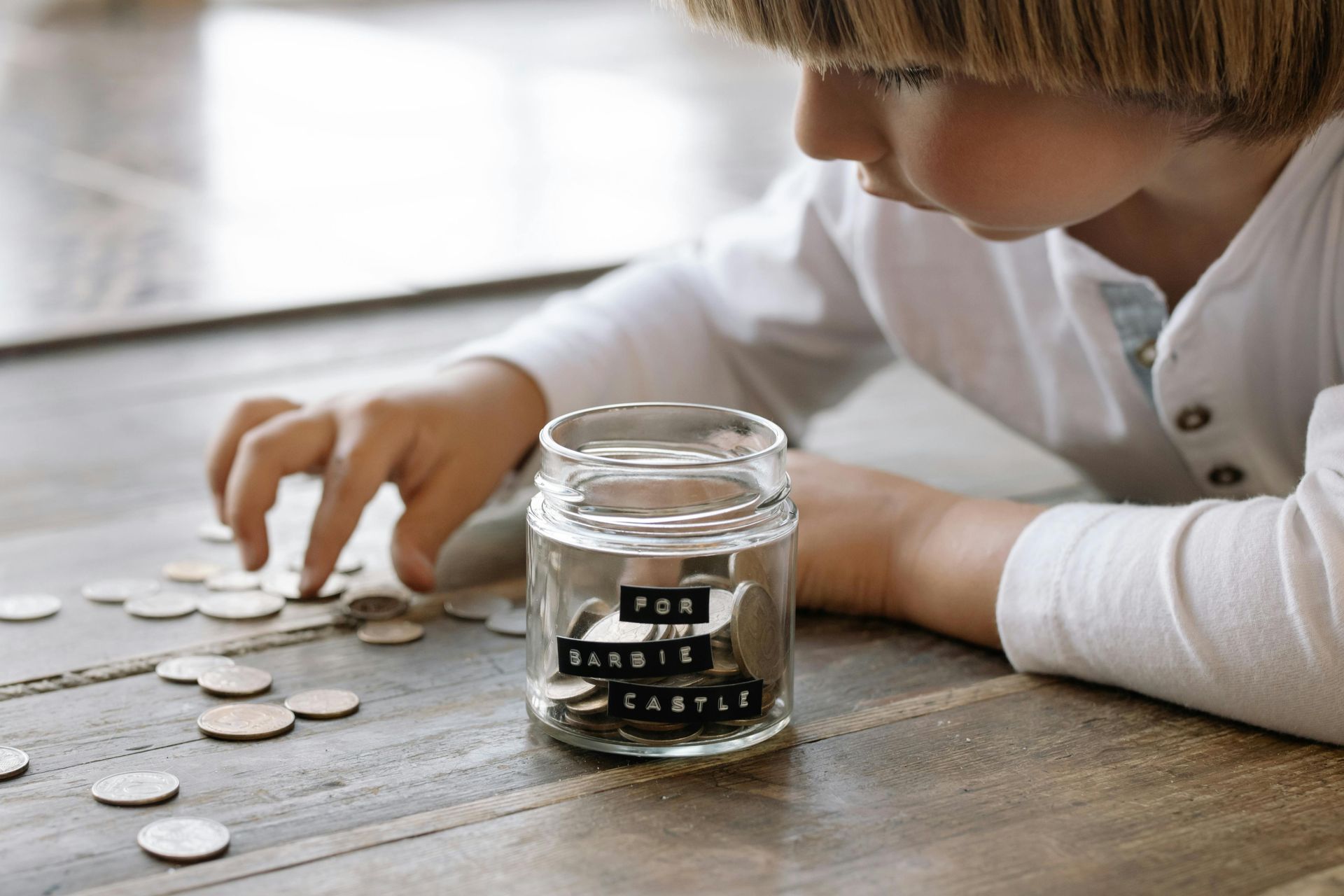 A young kid putting coins in a clear jar.