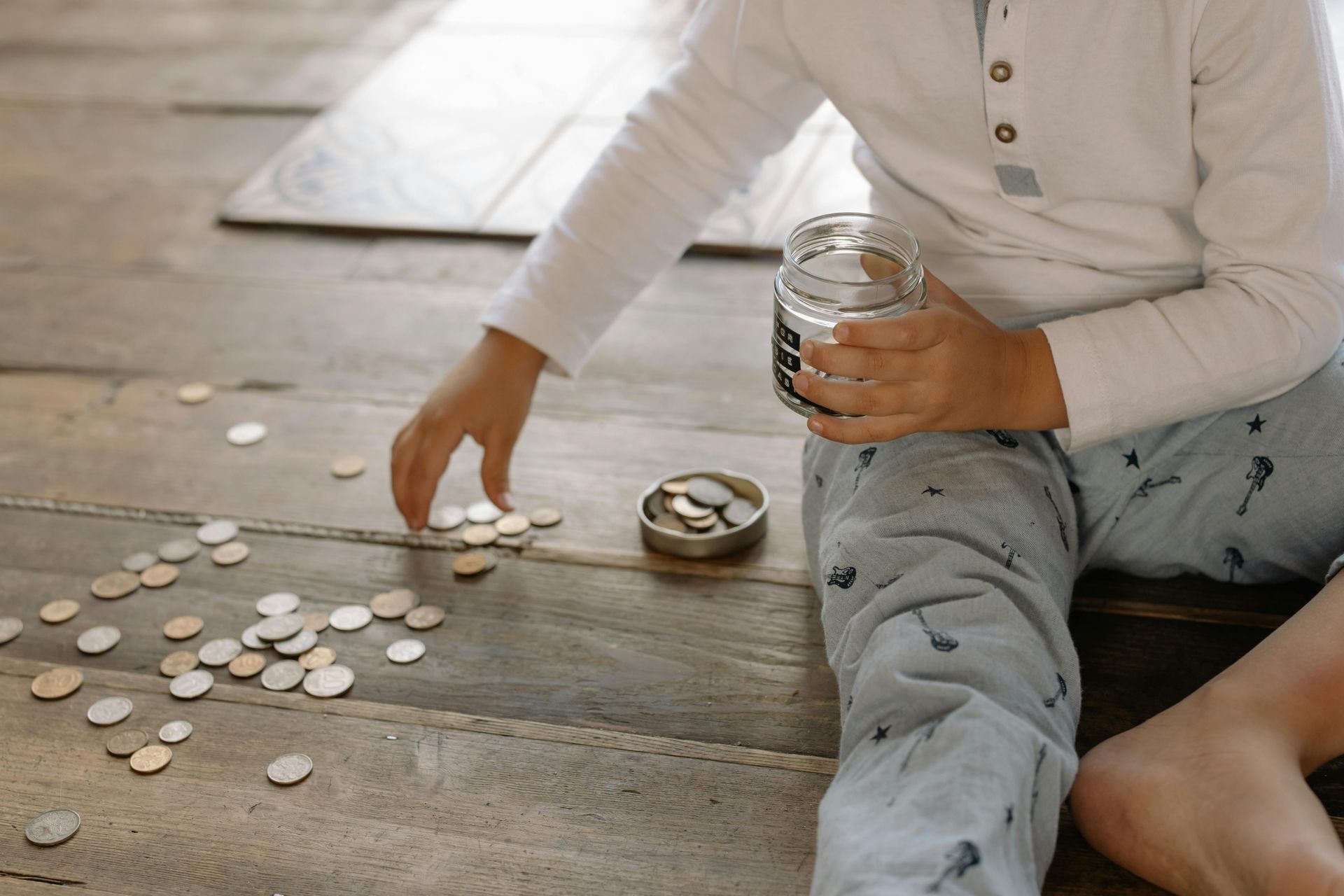 A kids counting coins and putting them into a jar.