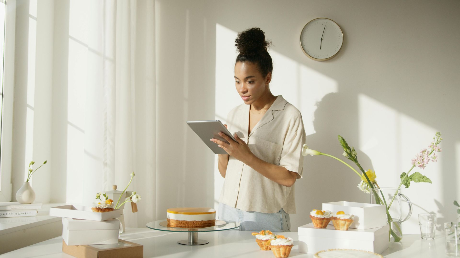 A girl on her iPad in front of a cake and cupcakes.