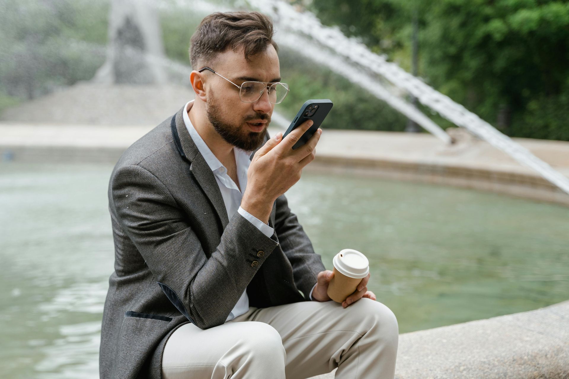 A man looking at his phone sitting in front of a fountain.