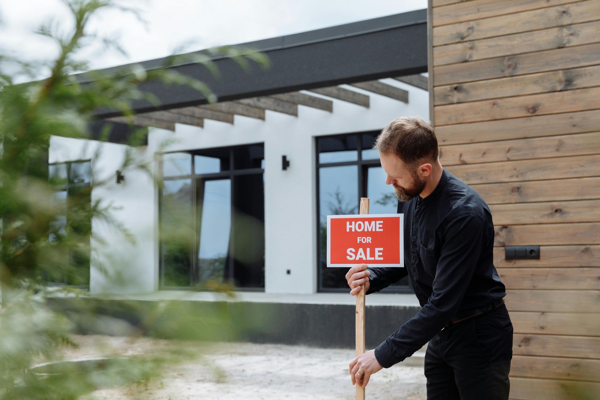 A man placing a red 'Home for Sale' sign in the yard.