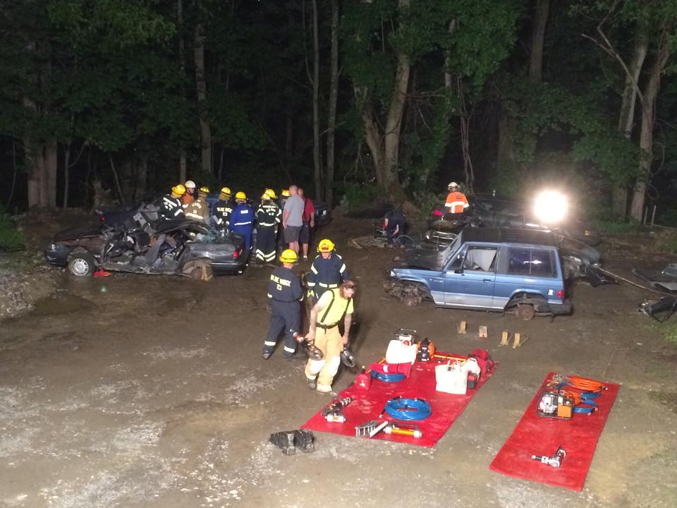 A group of firefighters are standing in front of a pile of cars.