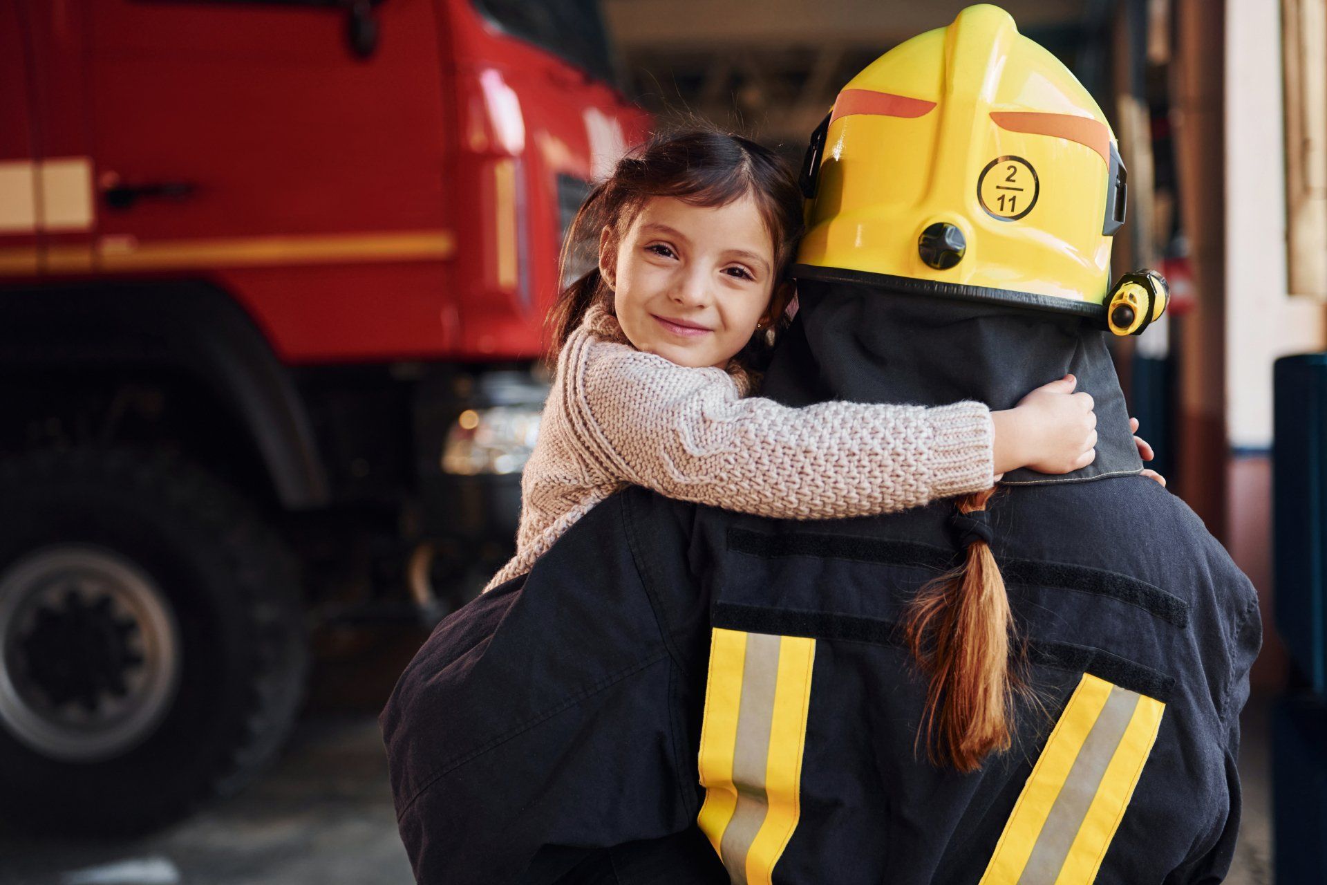 A firefighter is carrying a little girl on her shoulders.