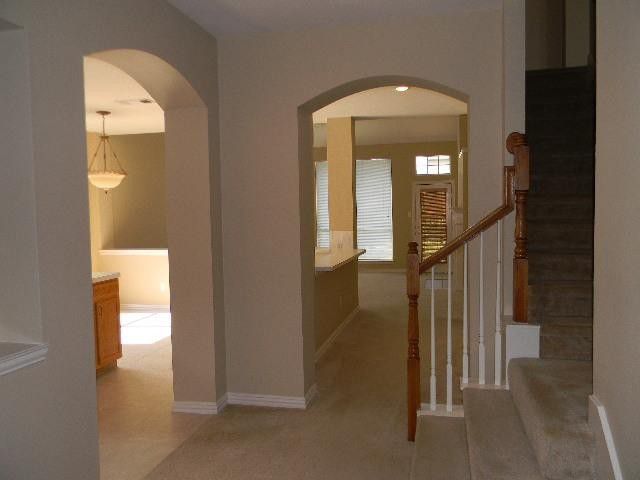 An entryway with beige walls, arched doorways leading to other rooms, and a carpeted staircase with a wood railing.