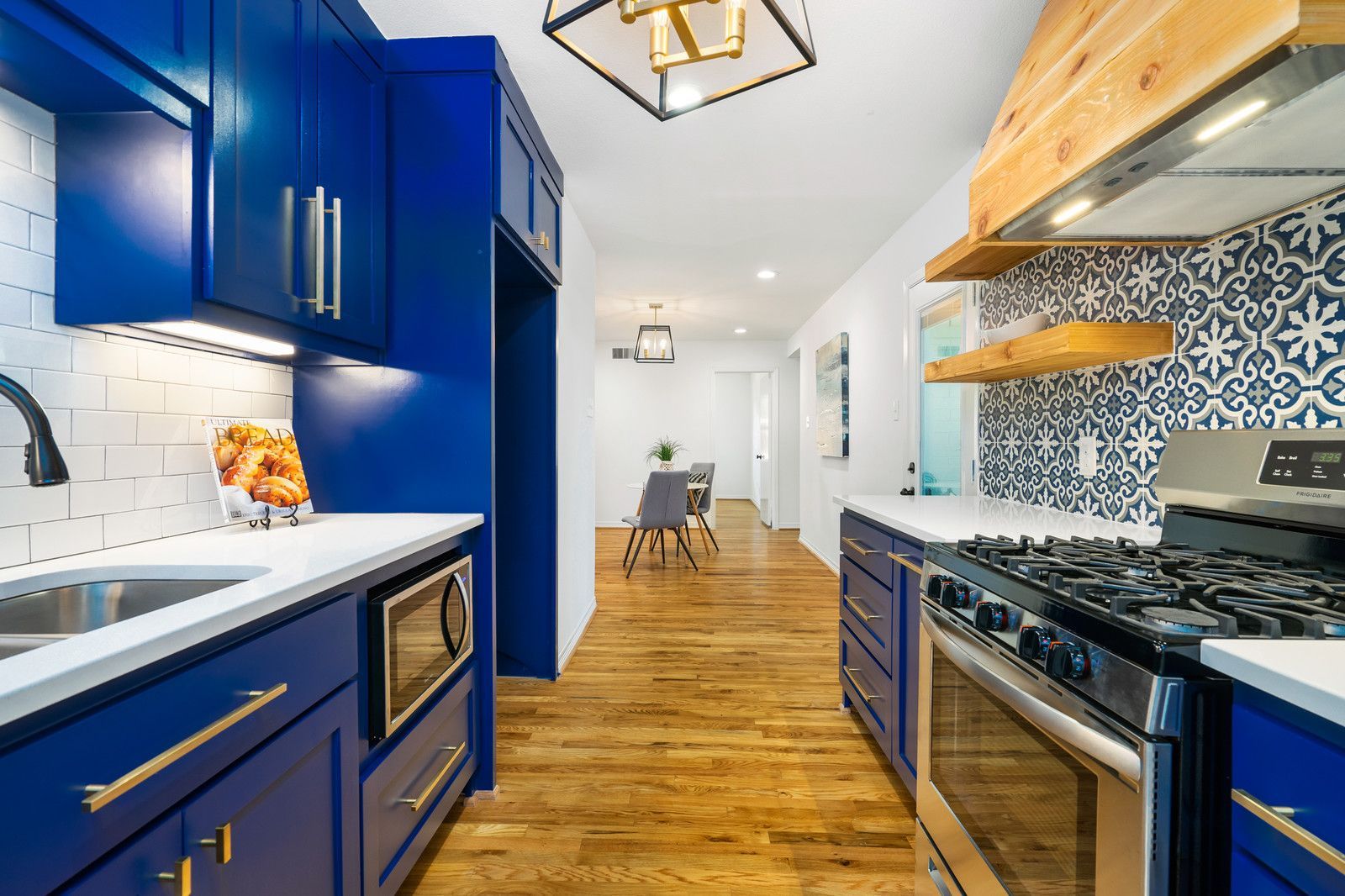 Modern galley kitchen with royal blue cabinets, white quartz countertops, stainless steel appliances, and a wood range hood.