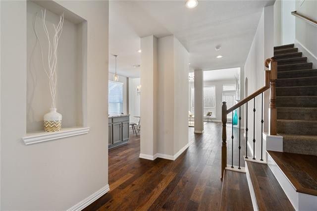 Interior view of an entryway with dark wood floors, a recessed wall niche with decor, and stairs with dark carpet.