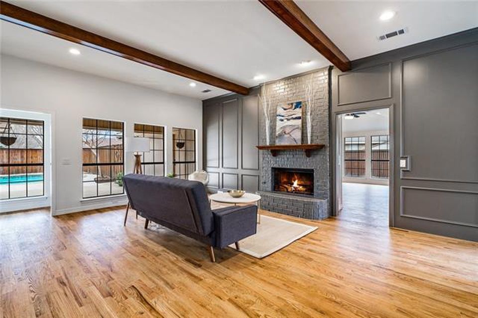 A modern living room with wood floors, a dark gray sofa, a fireplace with a stone facade, and large windows.