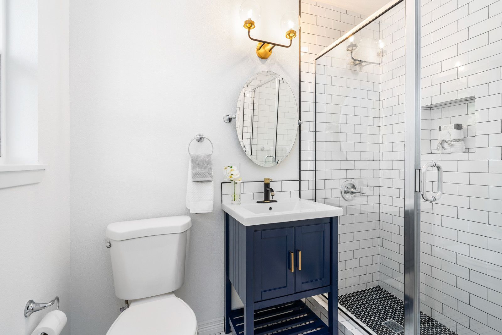 A modern bathroom with a navy blue vanity, white subway tile shower, oval mirror, and a white toilet.