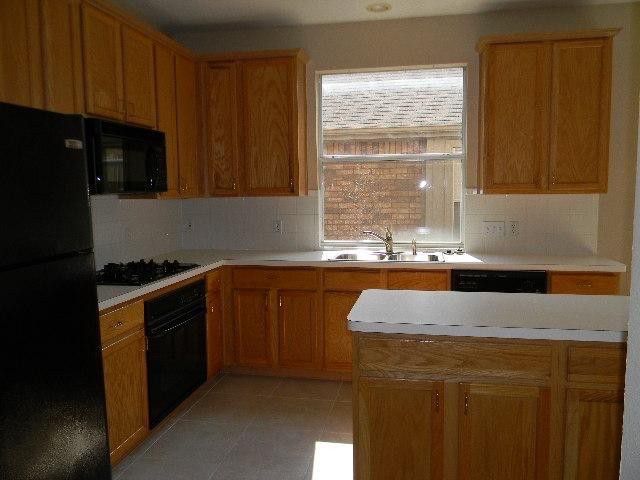 A kitchen with wood cabinets, black appliances, light countertops, and a window above the sink.