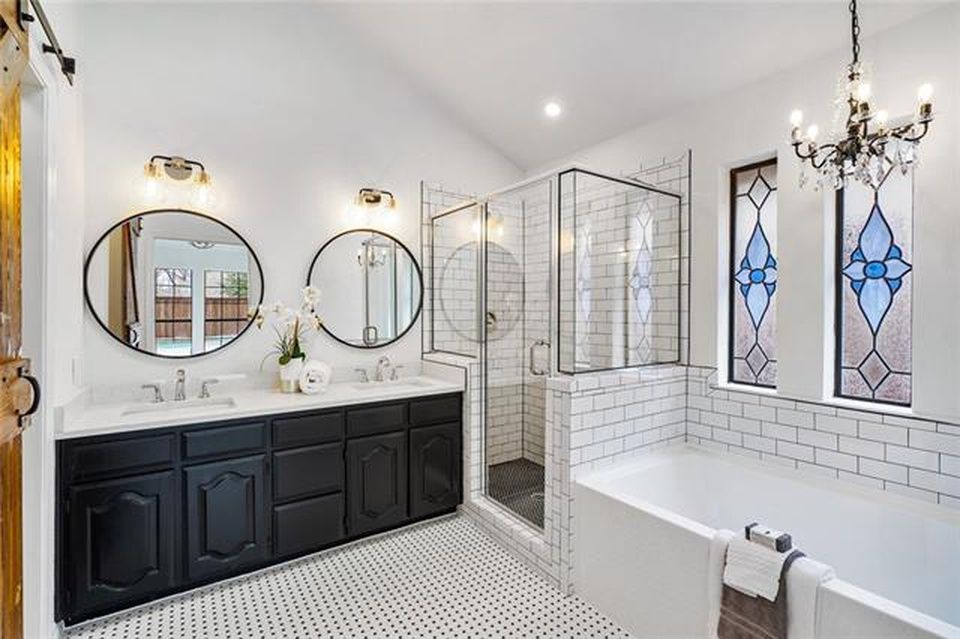 Modern farmhouse bathroom with a black double vanity, white subway tile shower, soaking tub, and stained glass windows.