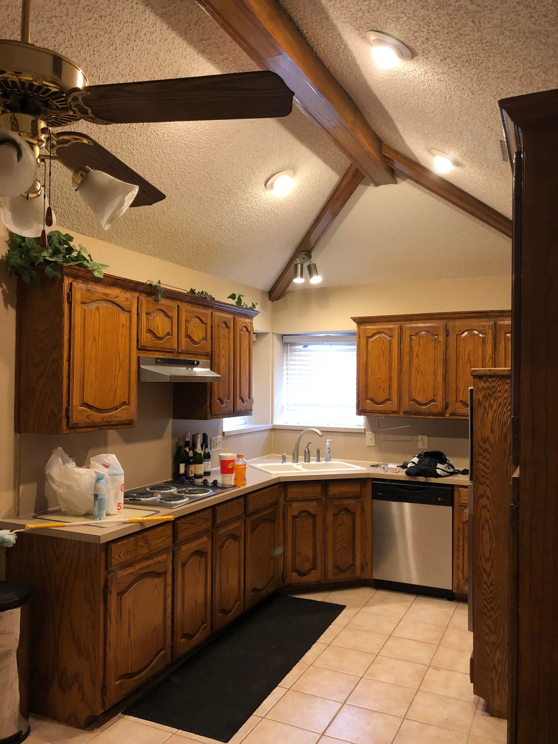 A kitchen with oak cabinets, a vaulted ceiling with wooden beams, a ceiling fan, and tiled floors.