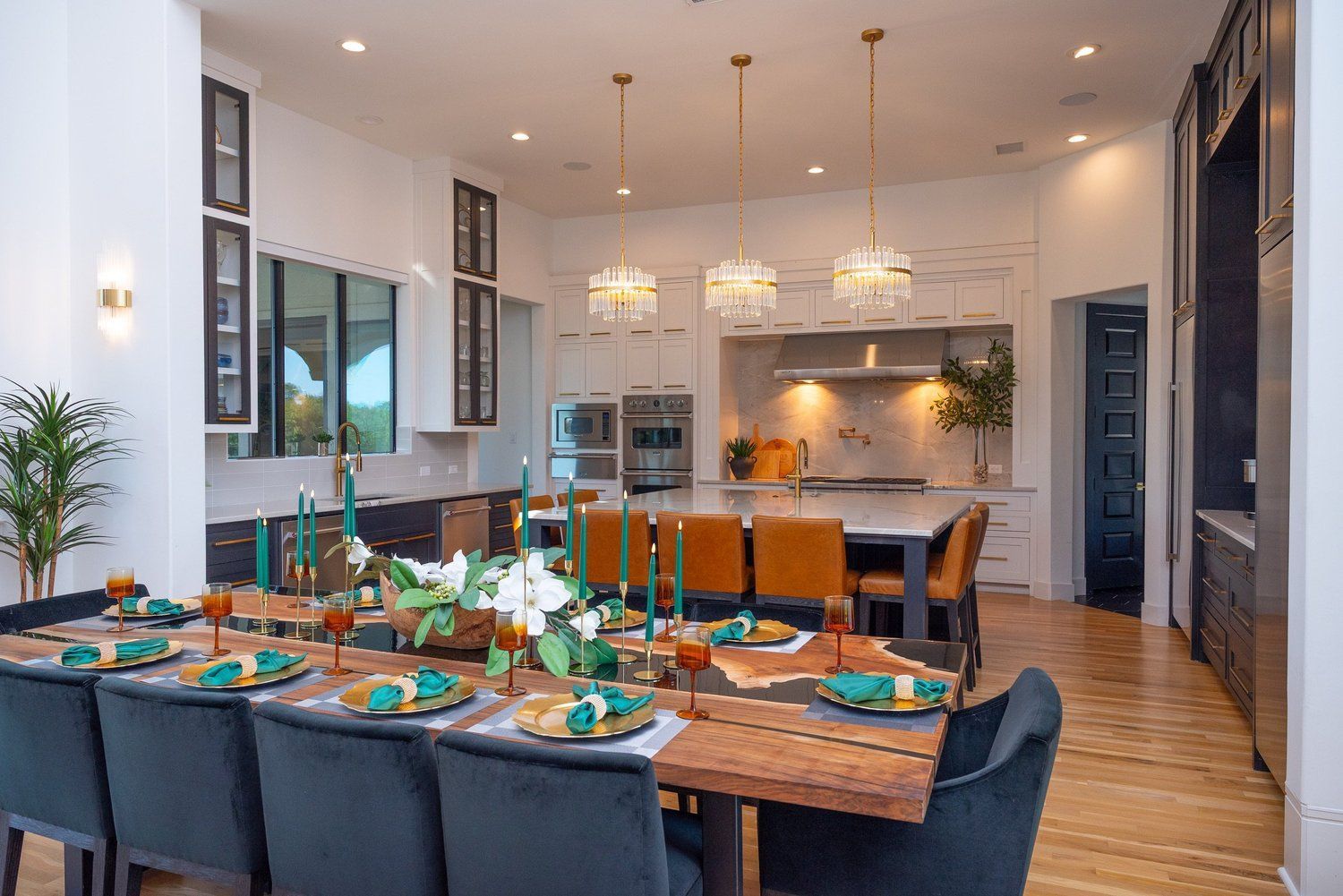 A dining table set for a meal sits in the foreground of a modern kitchen with white cabinets, wood floors, and island.