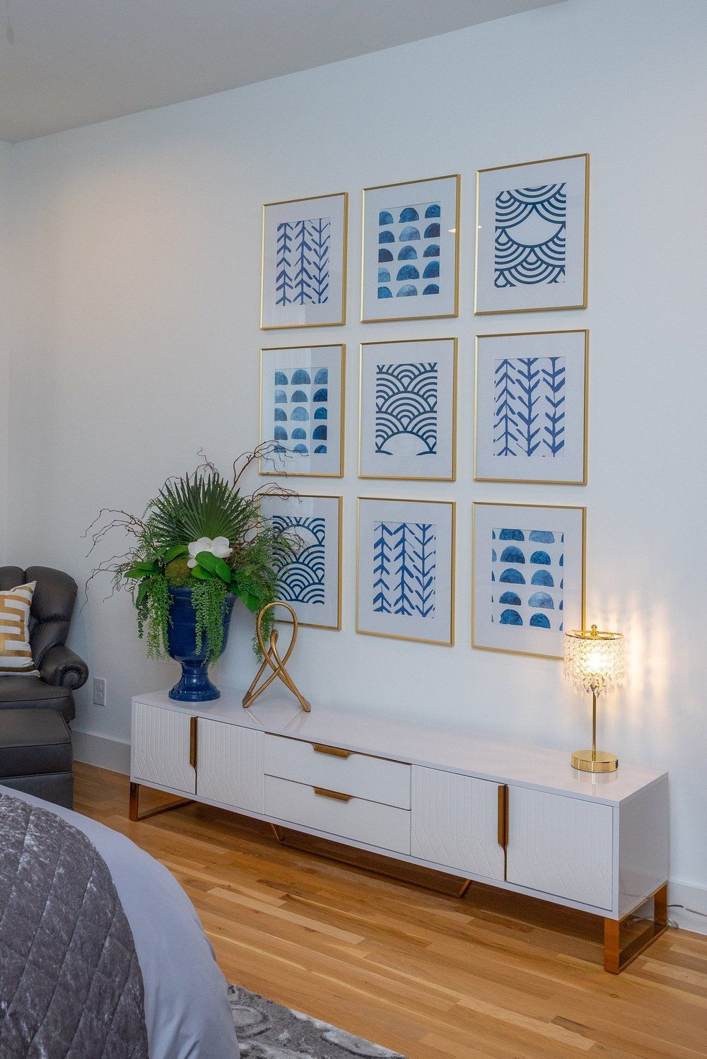 A white console table sits below a grid of nine blue and white framed art prints on a white wall in a room.