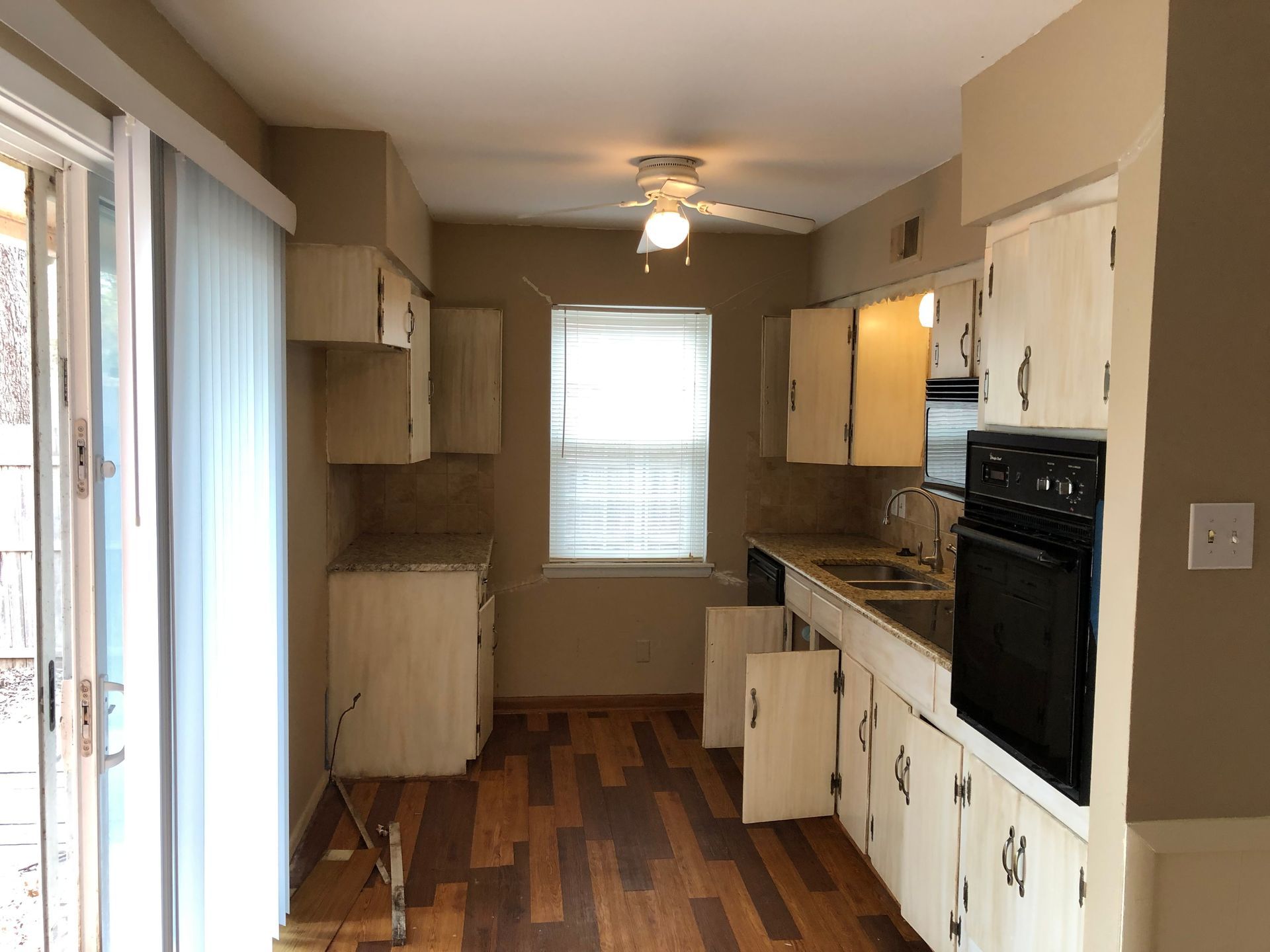 A kitchen with wood-look floors, beige walls, white cabinets, a black wall oven, and a sliding glass door.