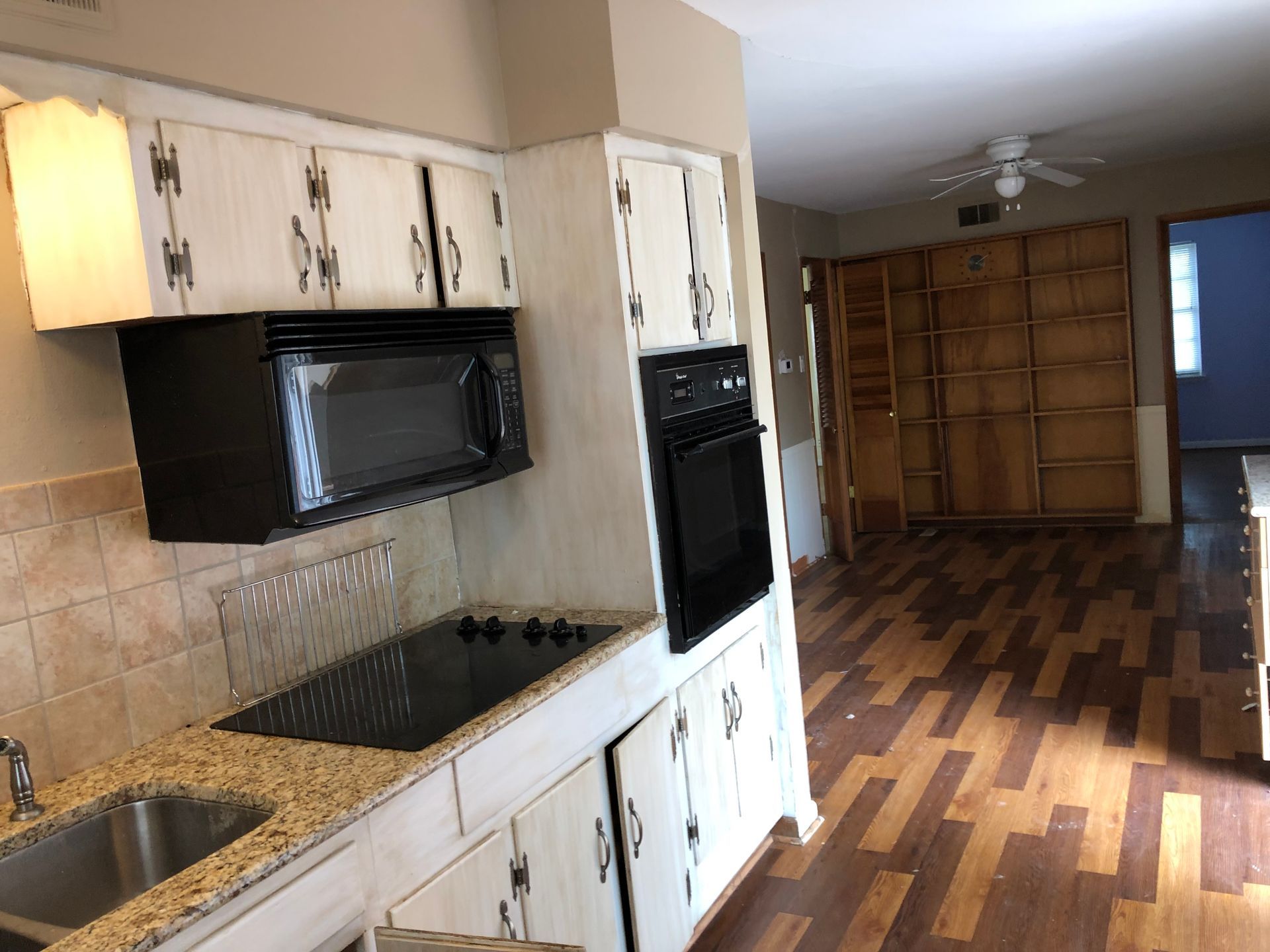 A kitchen with cream cabinets, a black microwave, a wall oven, a granite countertop, and wood-patterned flooring.