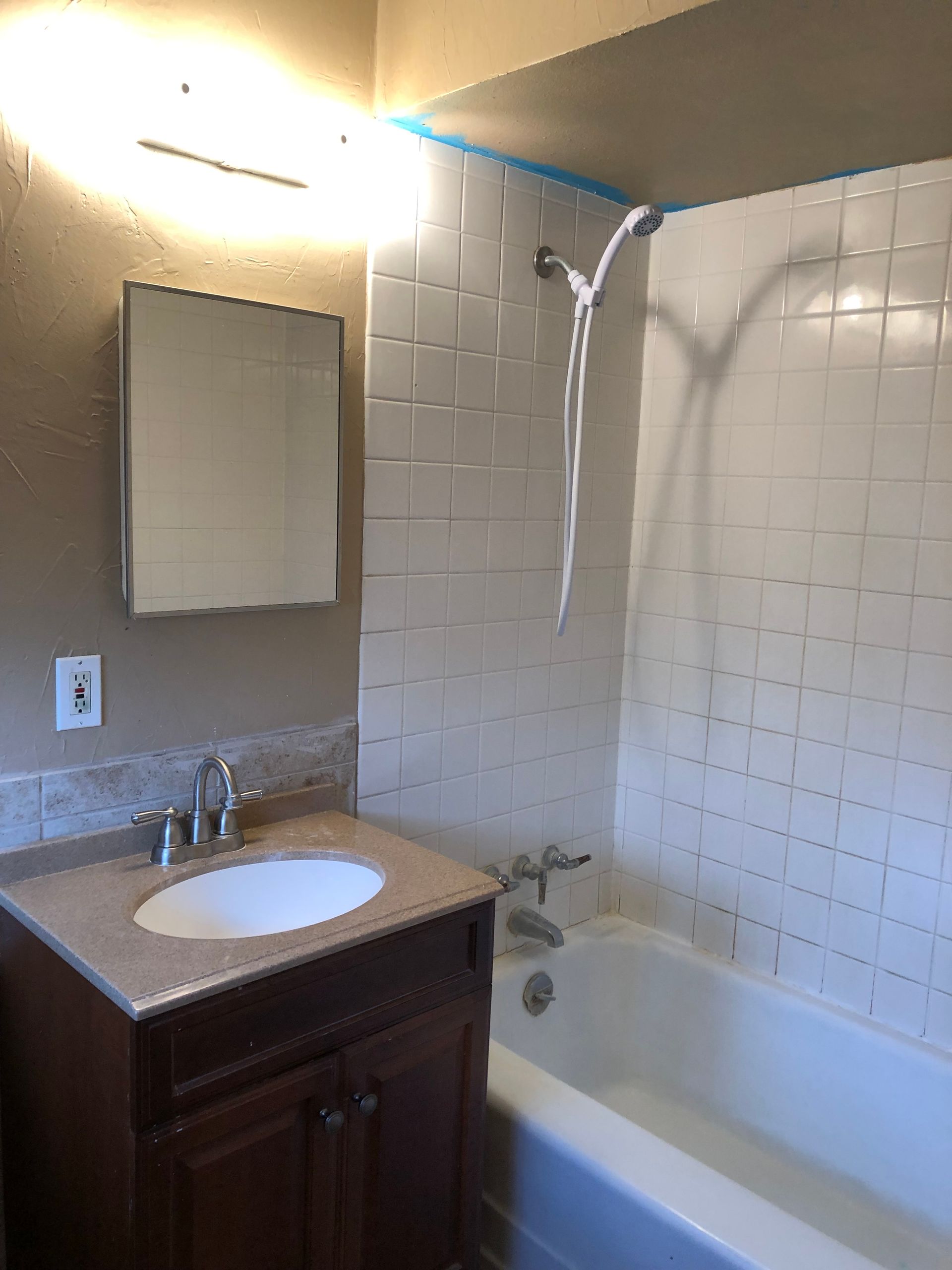 A bathroom featuring a dark wood vanity with a beige countertop, a white sink, a mirror, and a tiled shower-tub unit.
