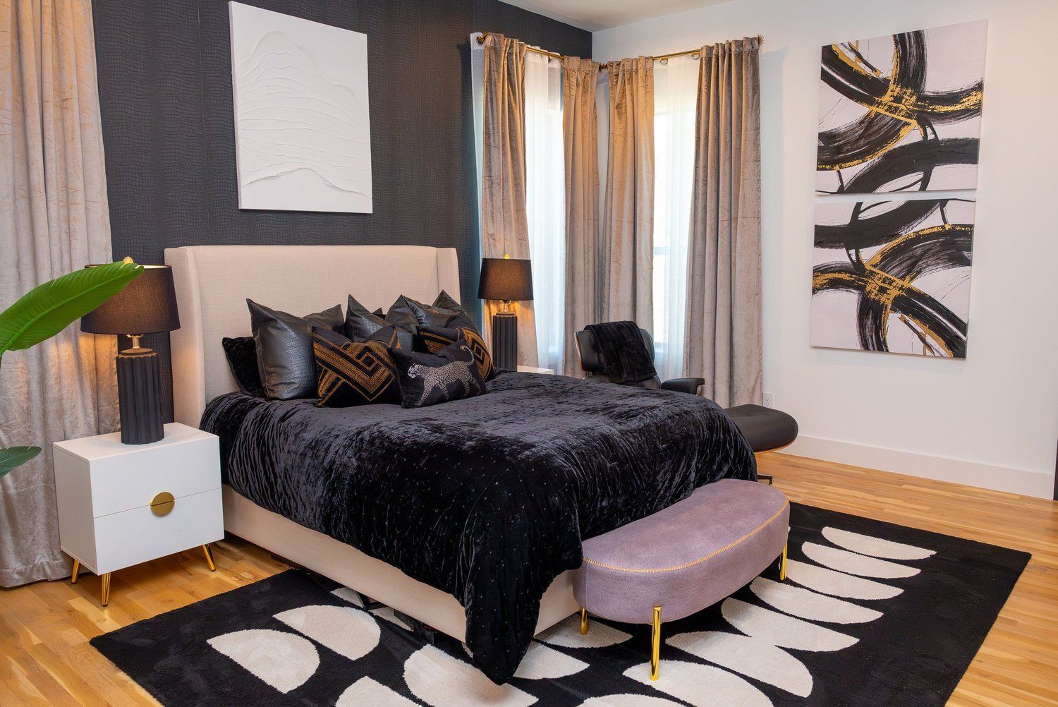 A bedroom featuring a beige tufted headboard, black bedding, a light purple bench, and a geometric patterned area rug.