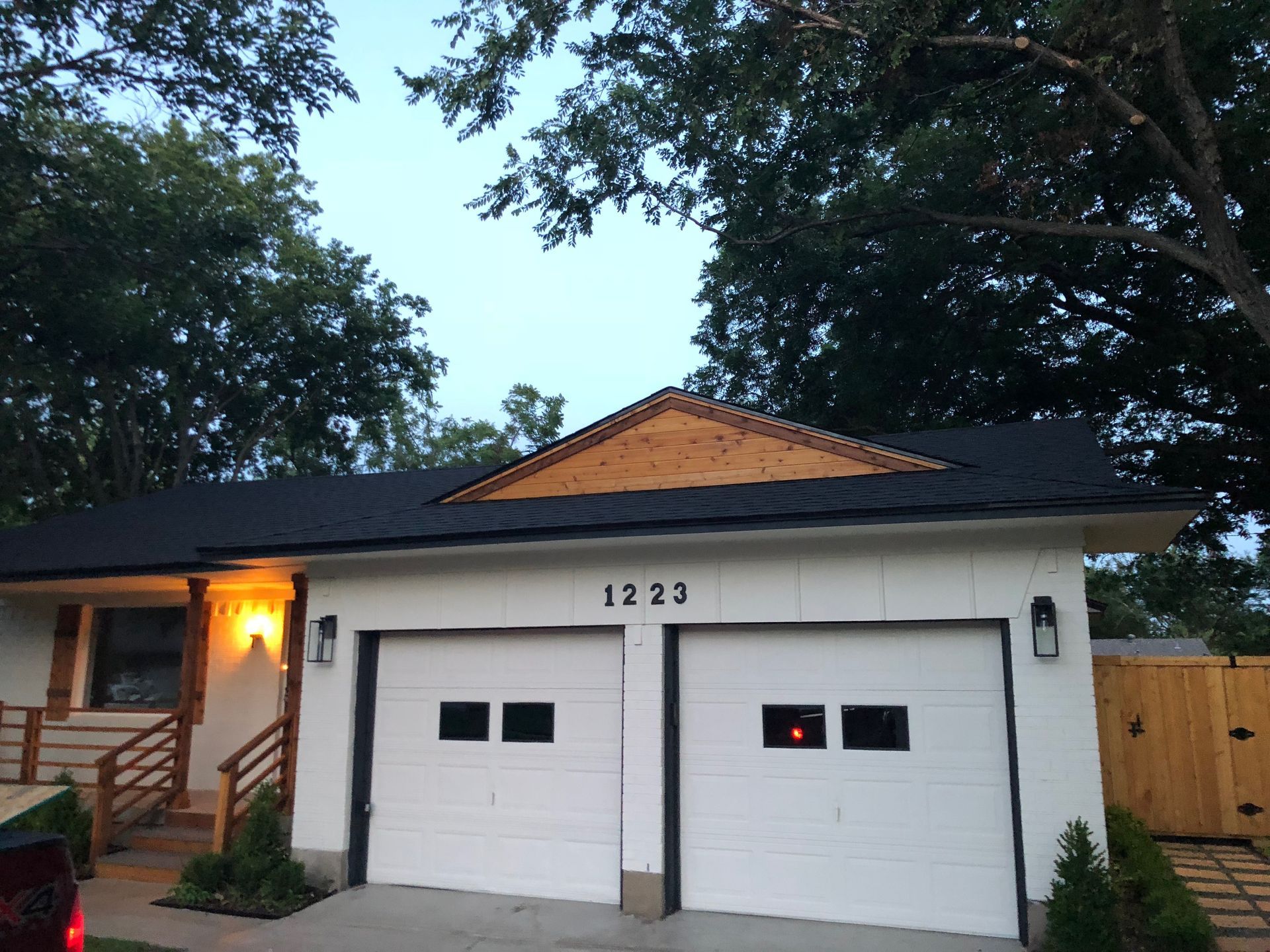 White house with two-car garage, black roof, and wood-paneled gable, with address number 1225 above the garage doors.
