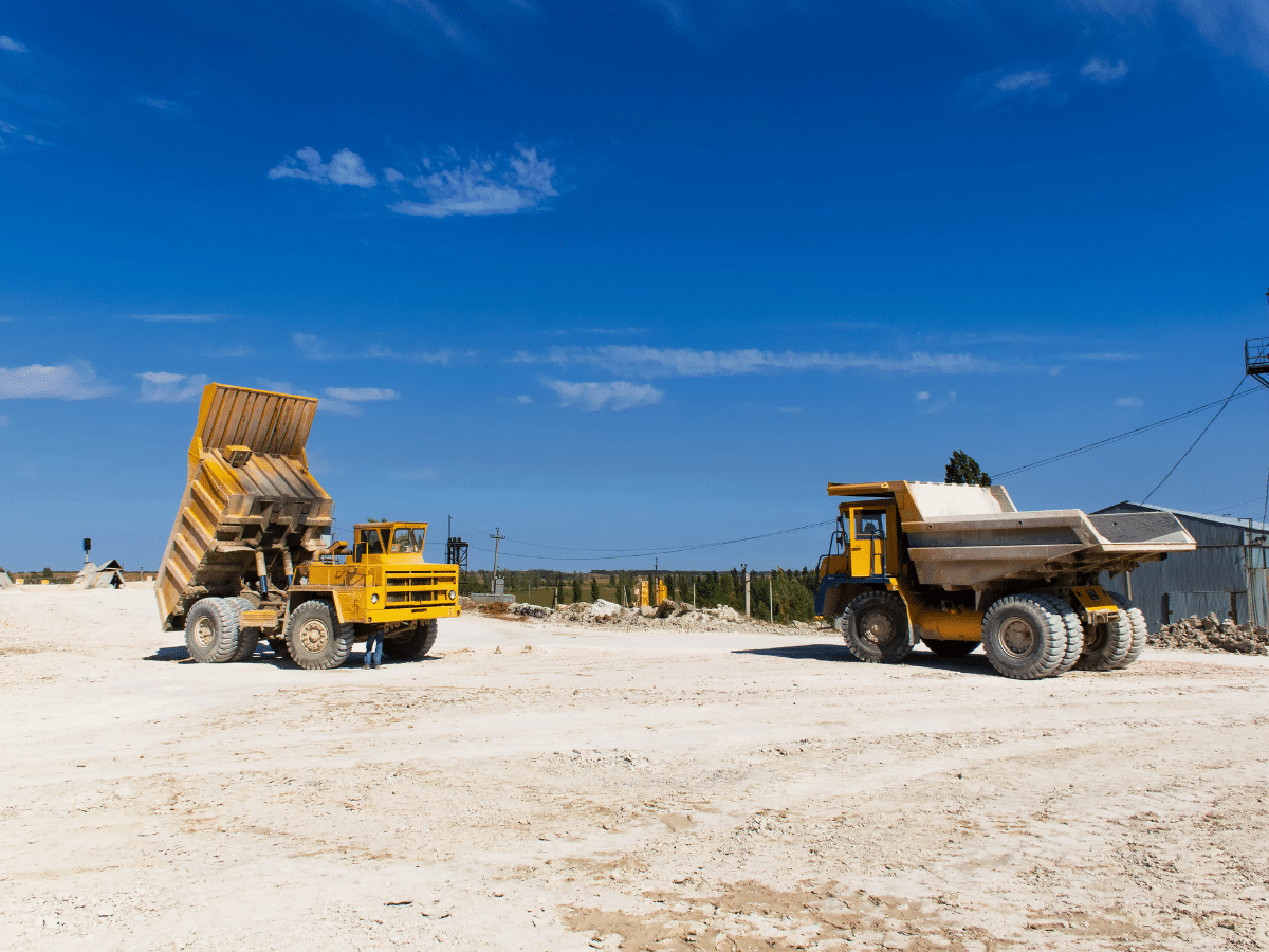 Two yellow dump trucks on a sandy quarry under a bright blue sky