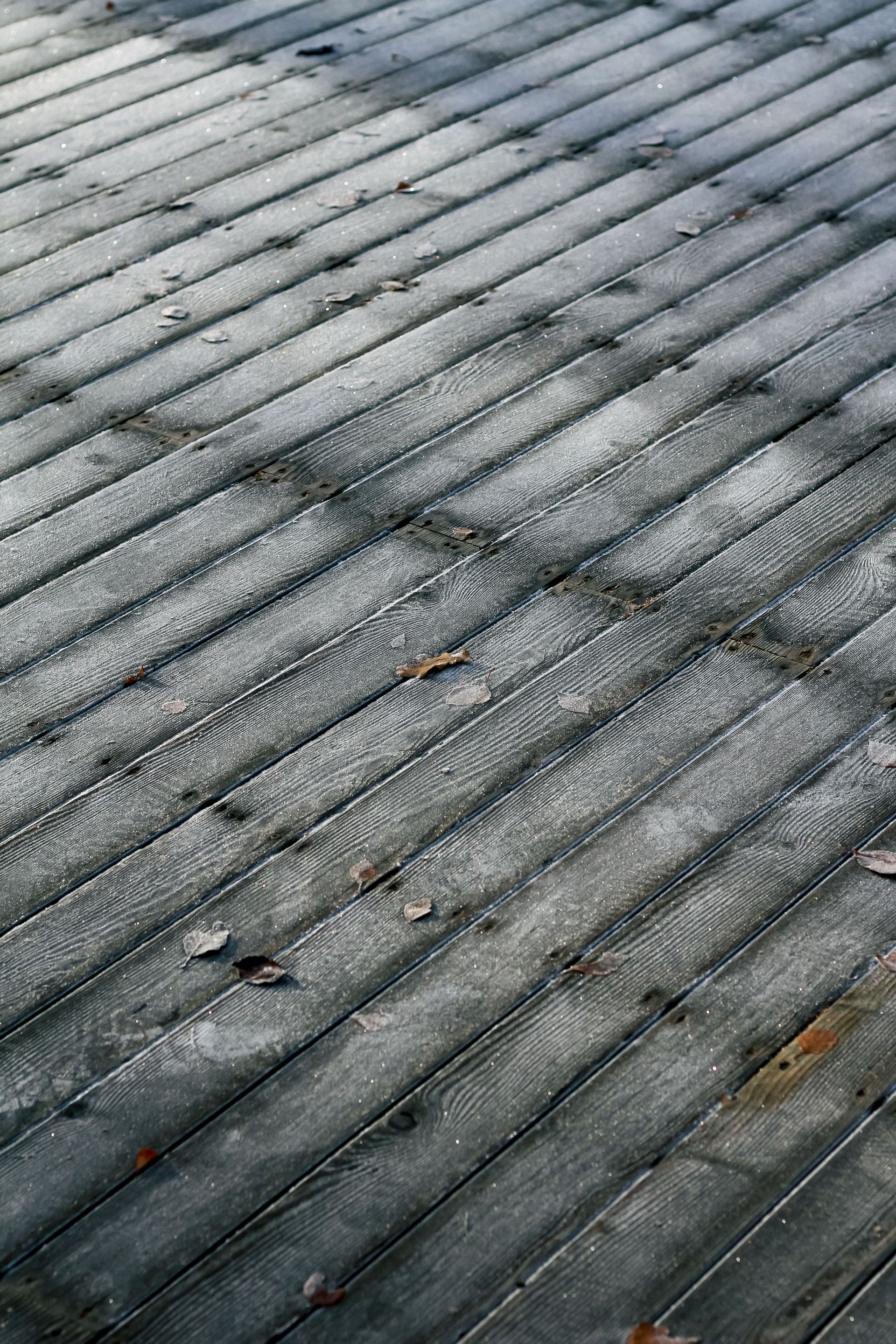 Weathered gray wooden deck boards with diagonal lines and scattered leaves