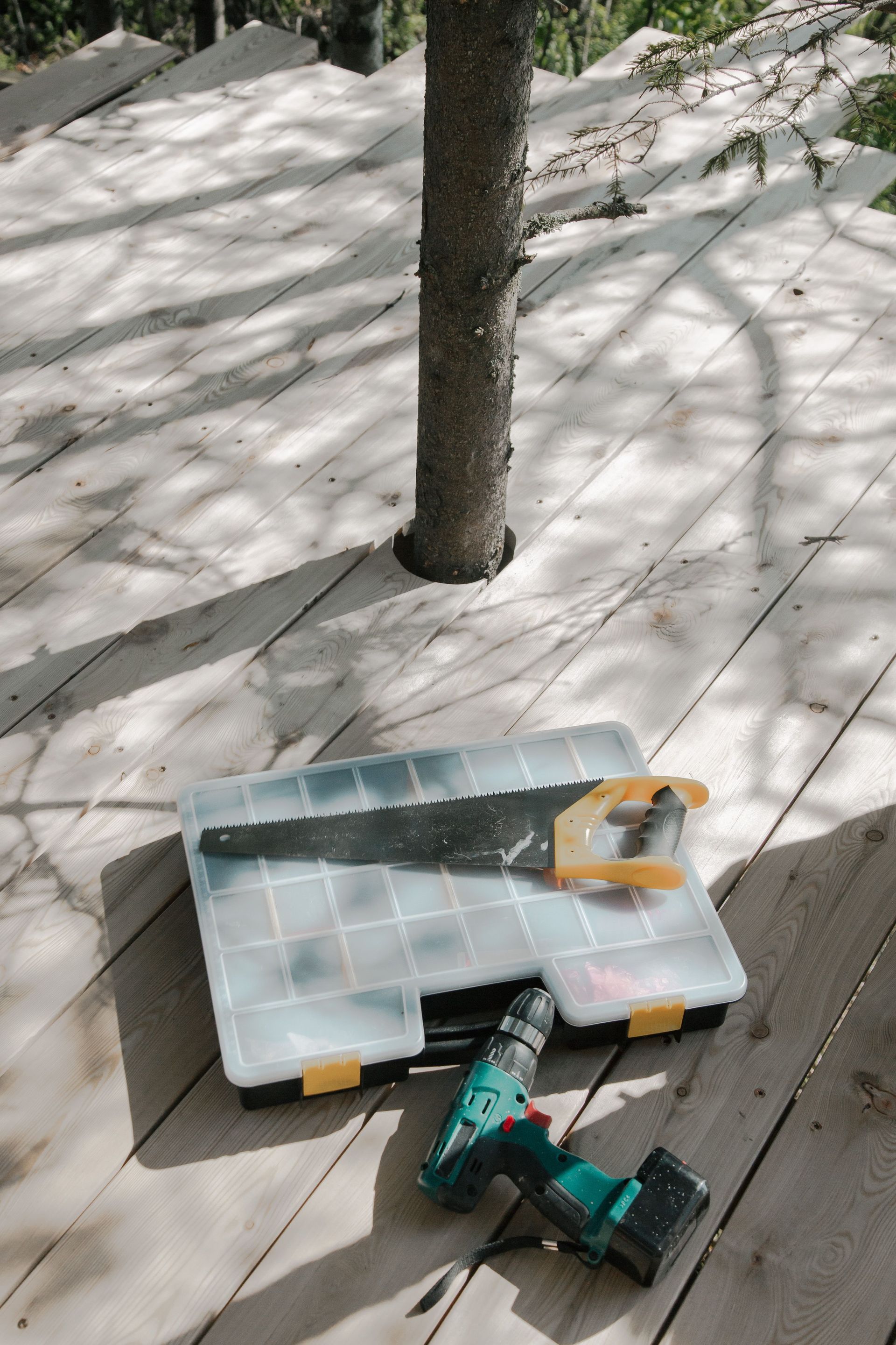 Tool case and green cordless drill on a wooden deck beside a tree in snow.