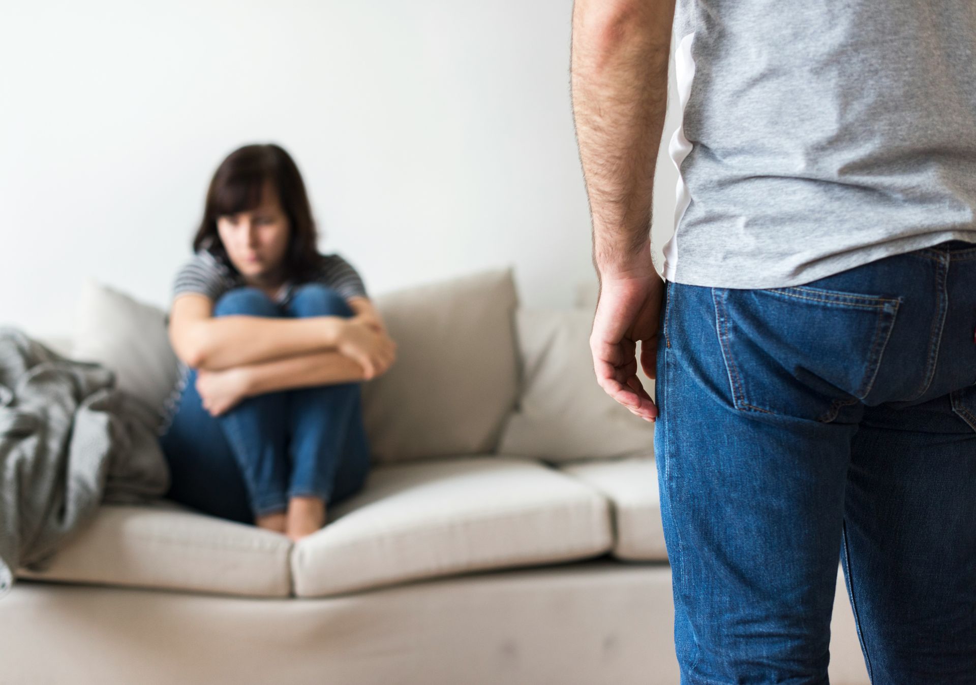A man is standing in front of a woman sitting on a couch.