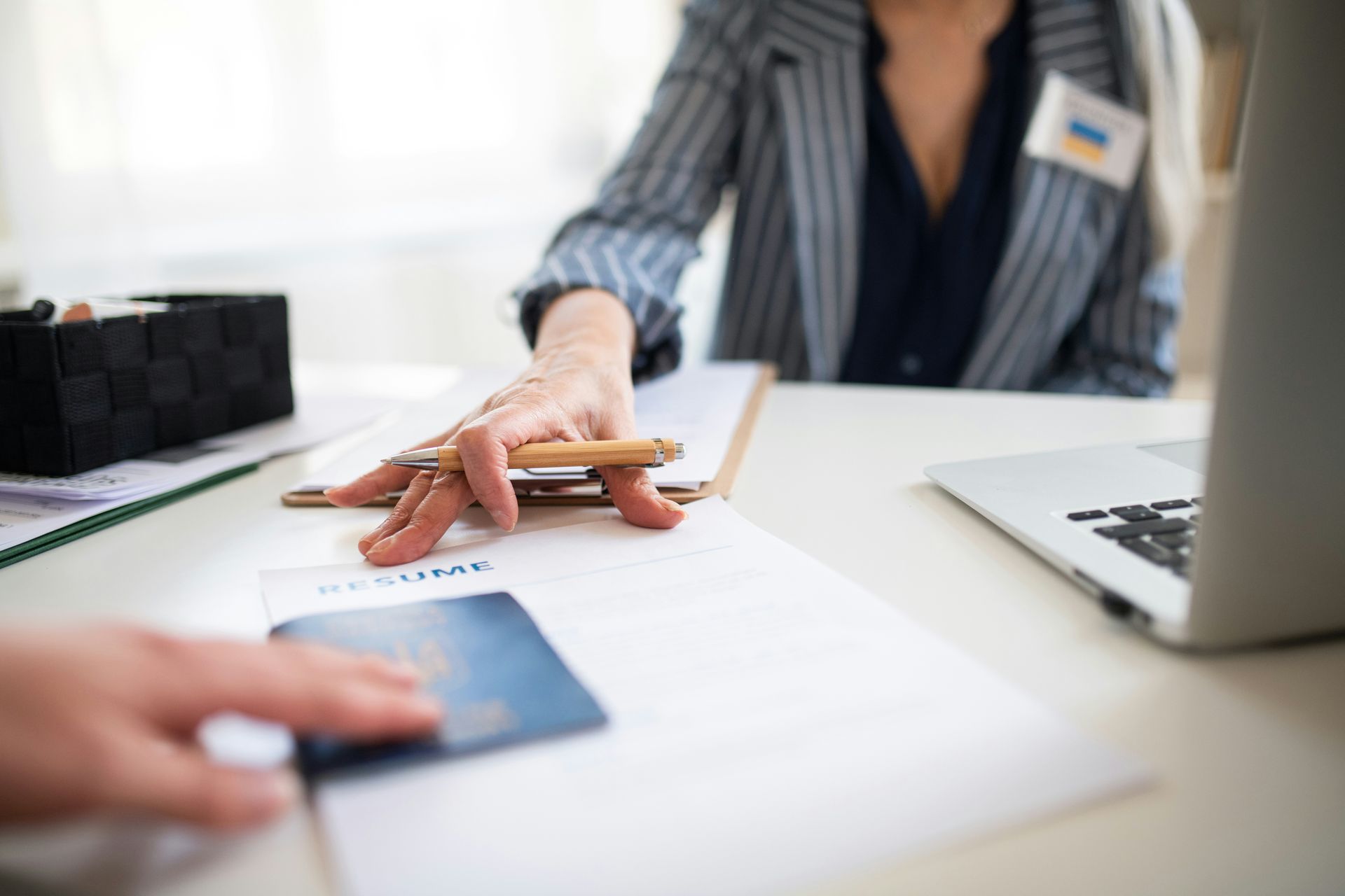 A woman is sitting at a desk with a laptop and a passport.