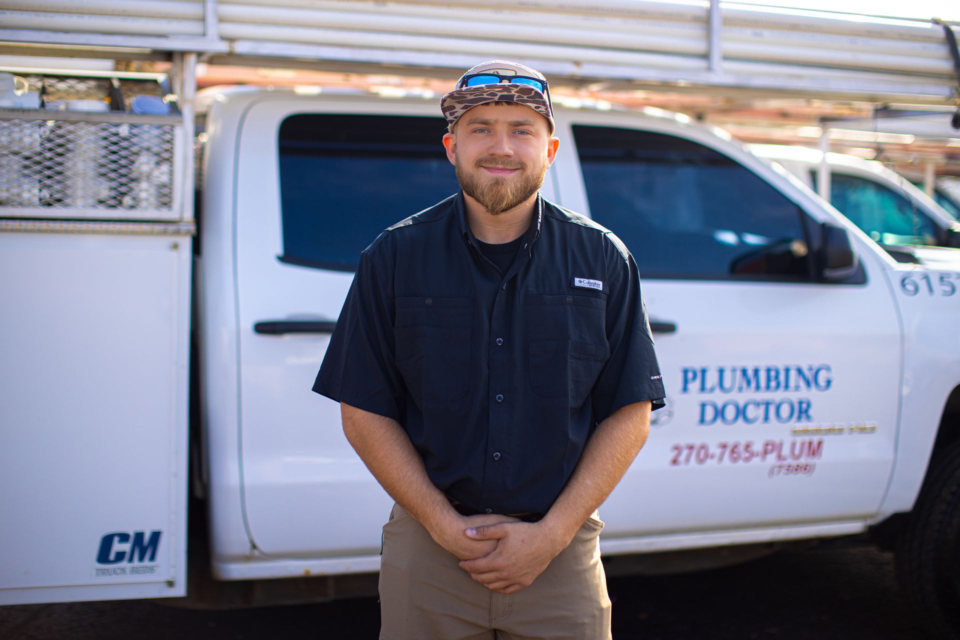 Plumber in blue shirt, standing in front of a white truck that says 